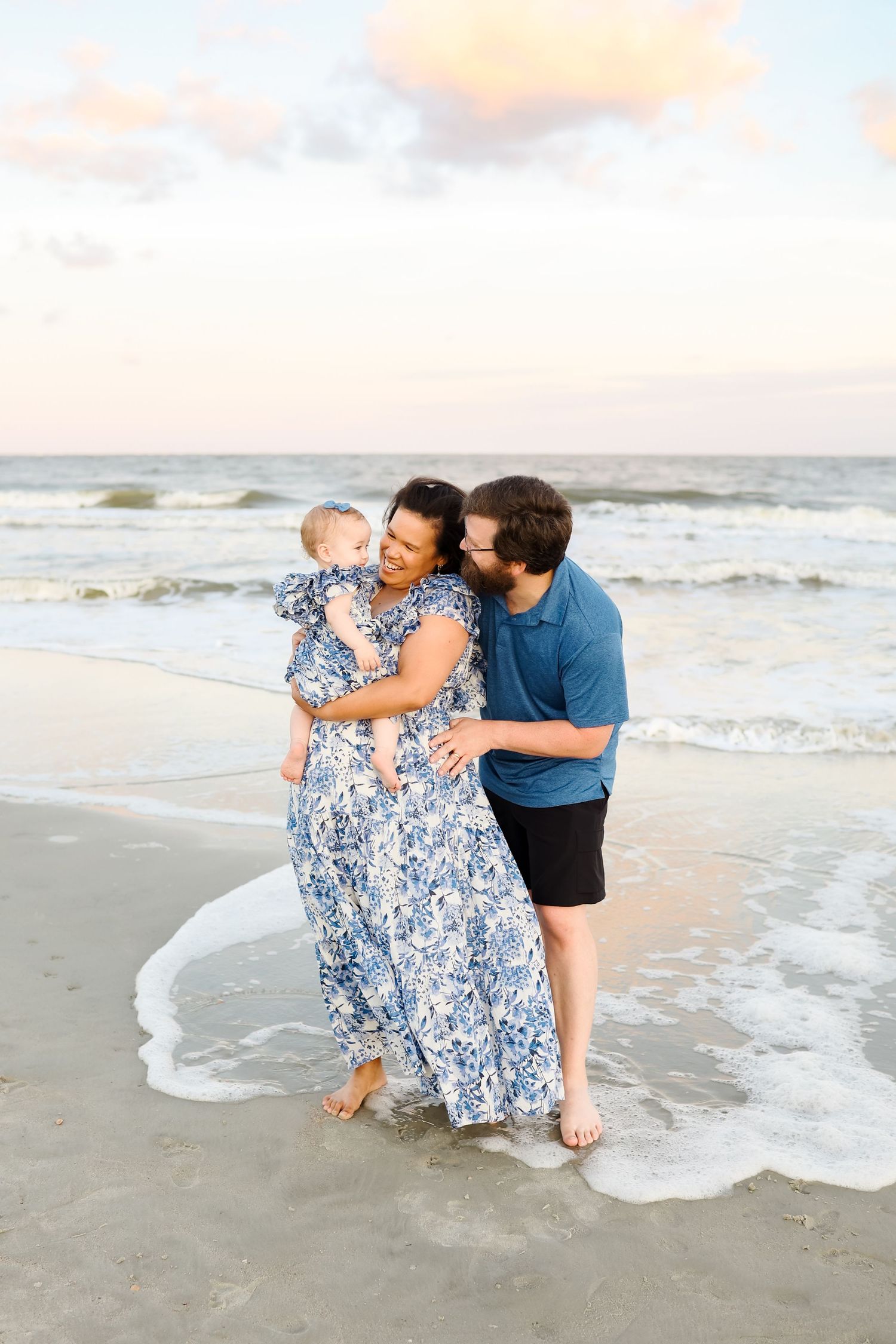 Beach family photos on Hilton Head with parents holding their baby daughter while standing in the ocean at sunset
