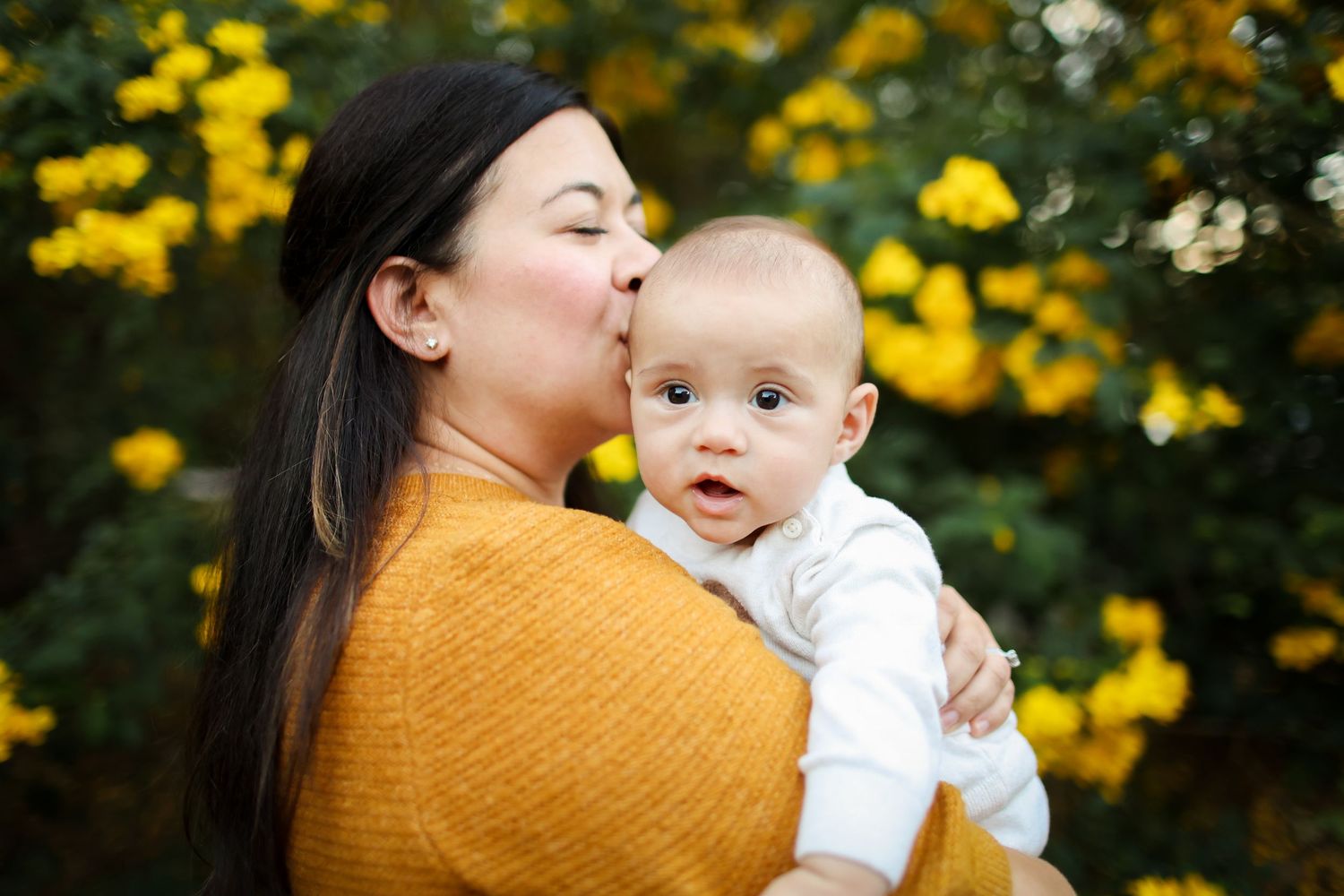 Hilton Head family photography capturing a mother kissing her newborn beside a blooming Winter Cassia tree on Hilton Head Island