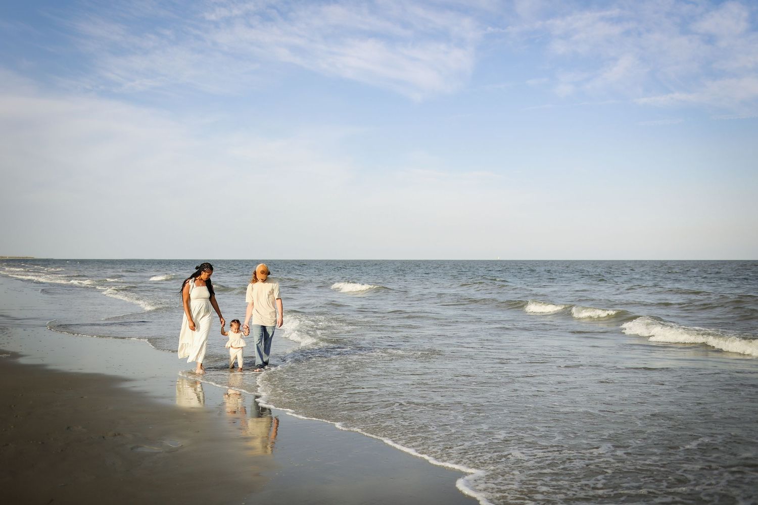 Hilton Head Island family photography with parents holding hands with their toddler walking along the shoreline at Driessen Beach