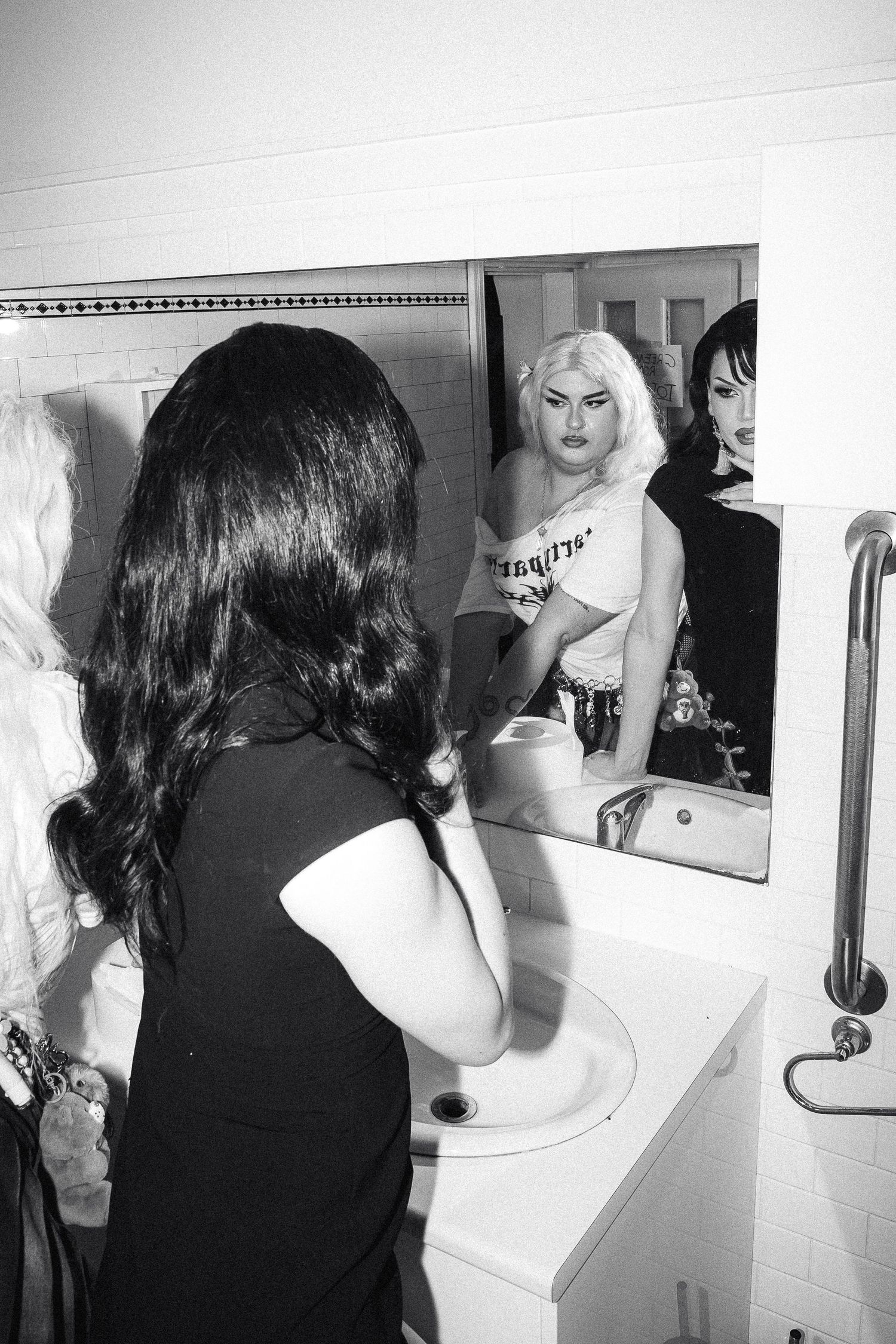 Black and white photo of people in bathroom mirror at The Lass O'Gowrie Hotel with drag queen.