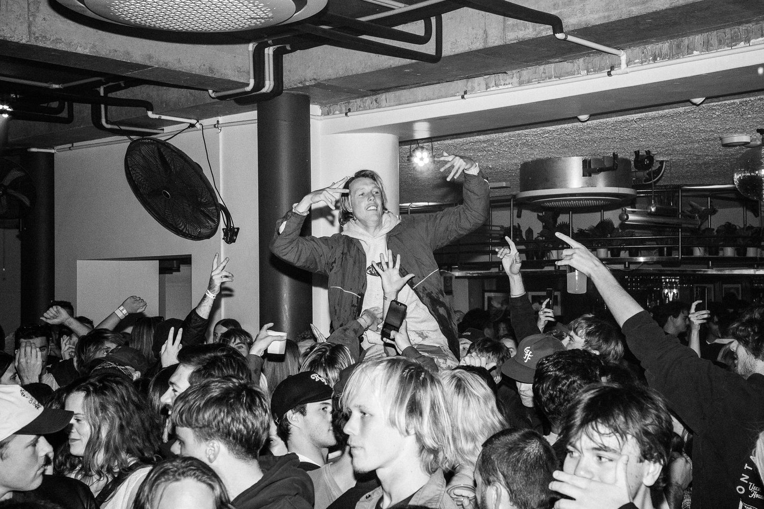 Black and white photo of energetic crowd at The Beach Hotel Merewether with performer elevated above audience.