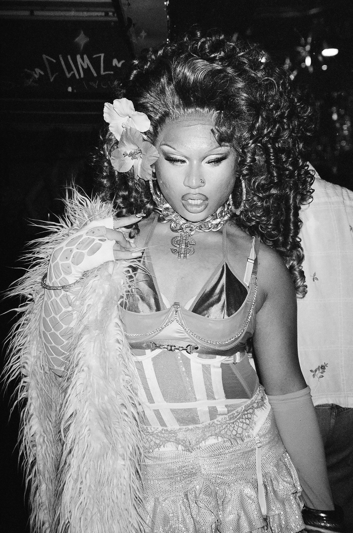 Black and white portrait of a drag performer in feather boa, corset, and dollar sign necklace The Lass O'Gowrie Hotel.