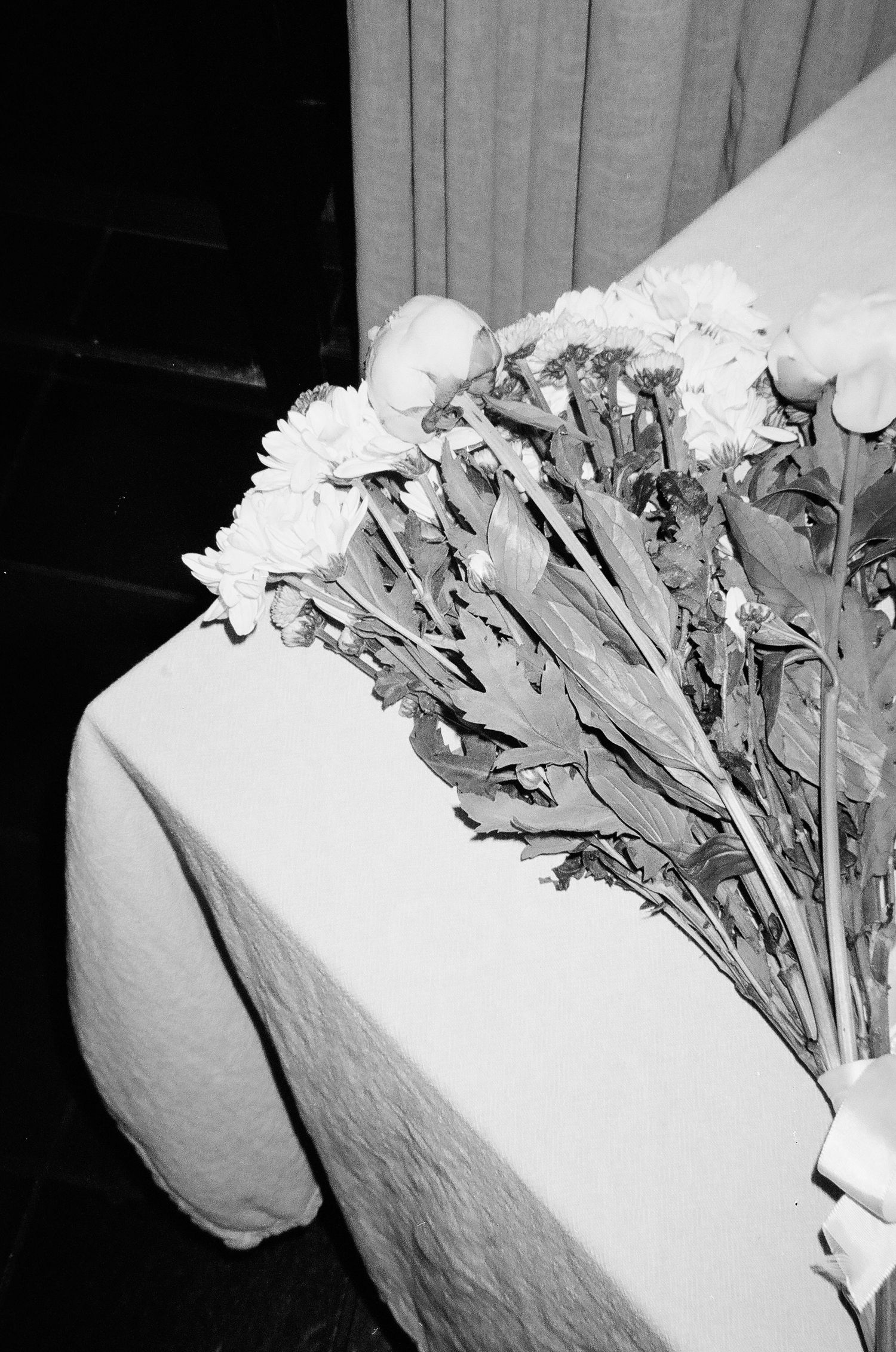 Black and white photo of wilting flower bouquet resting on white linen tablecloth at wedding reception.