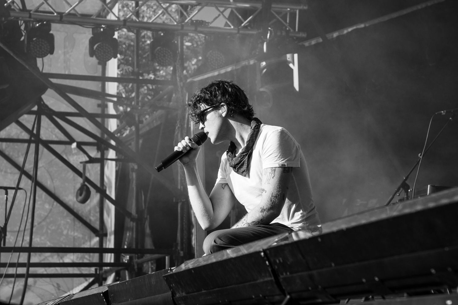 A male singer of San Cisco performs on stage holding a microphone under smoky black and white stage lighting.