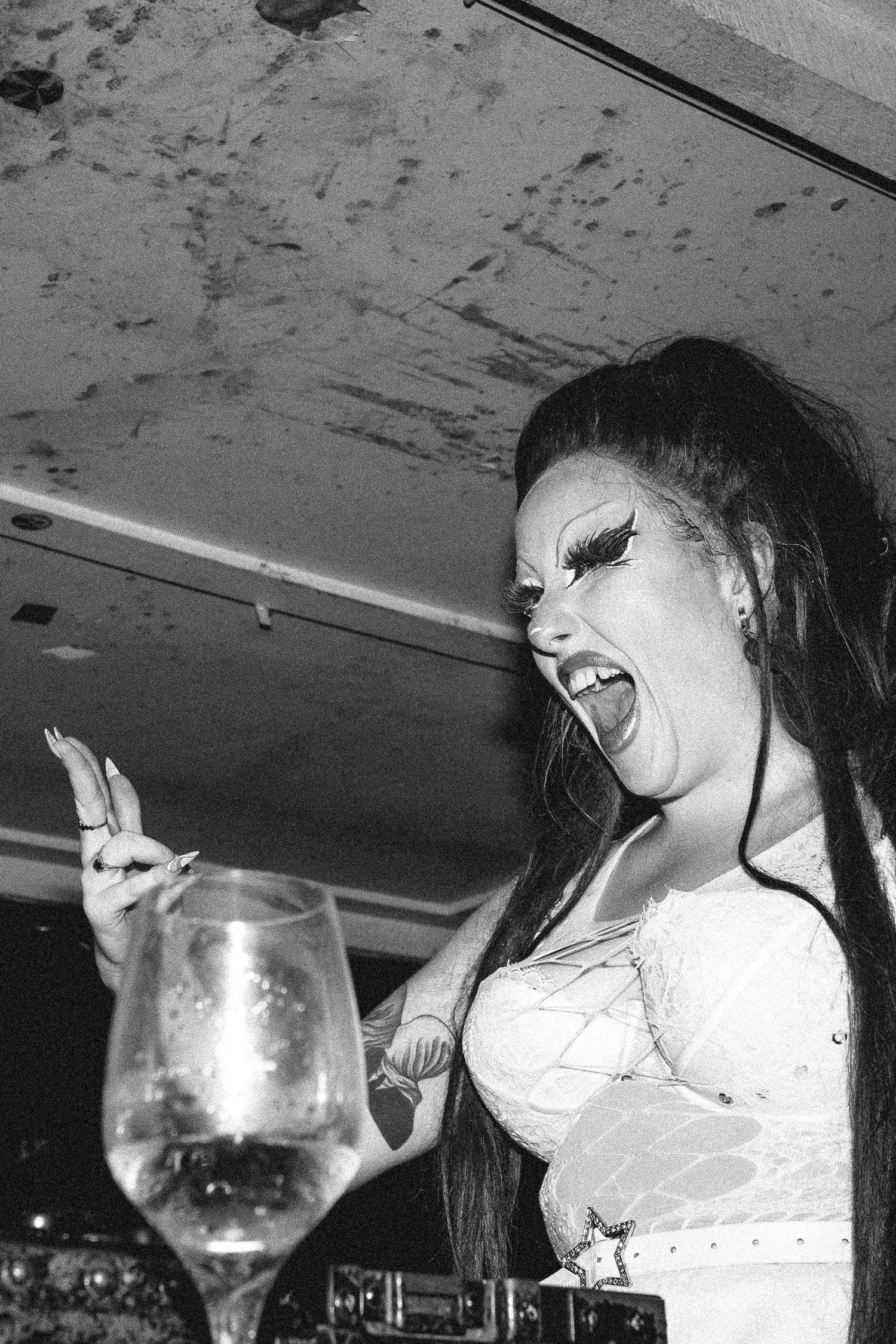 Black and white photo of woman in white dress laughing with wine glass at party.