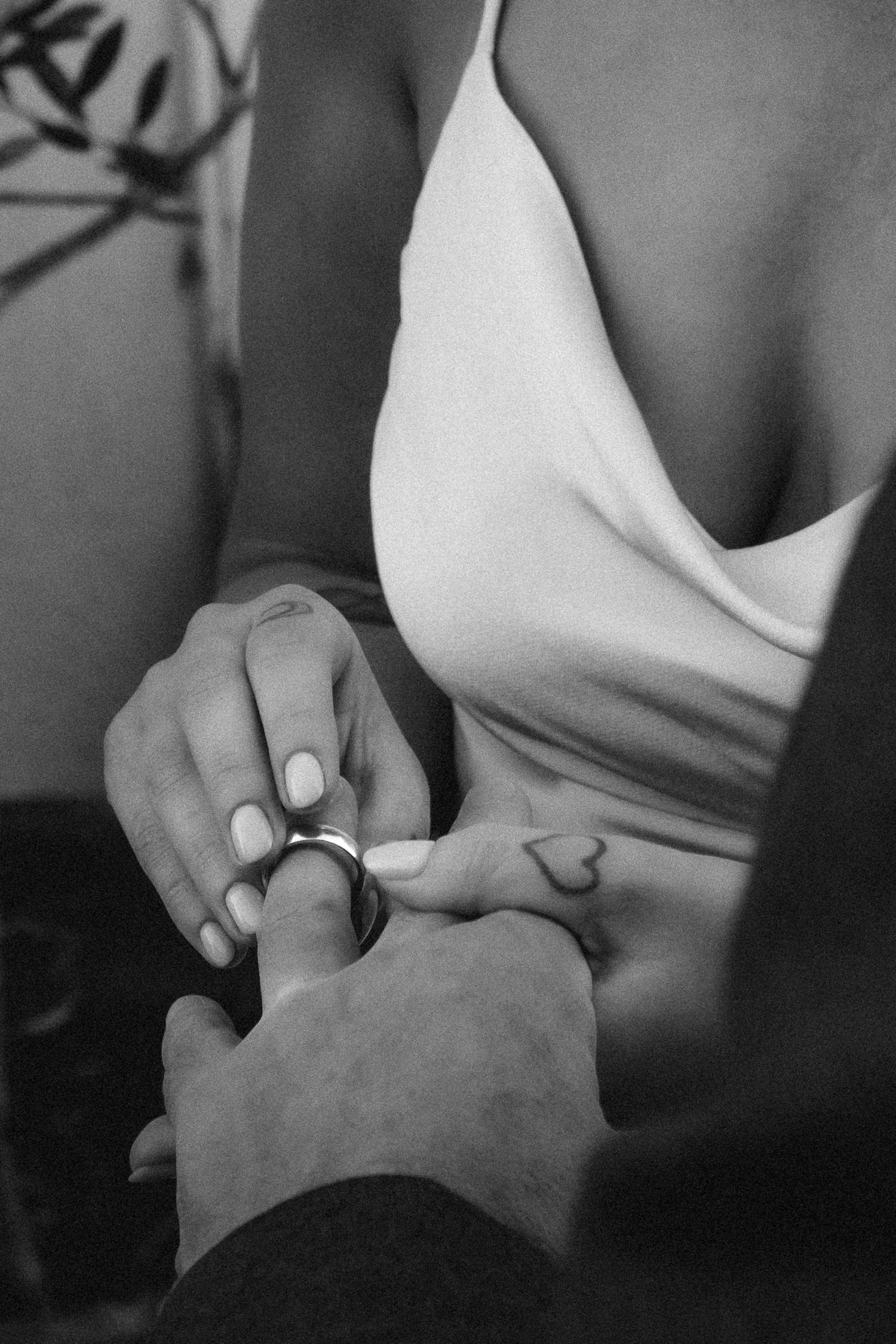 Black and white close-up of wedding ring exchange with heart tattoo visible on bride.