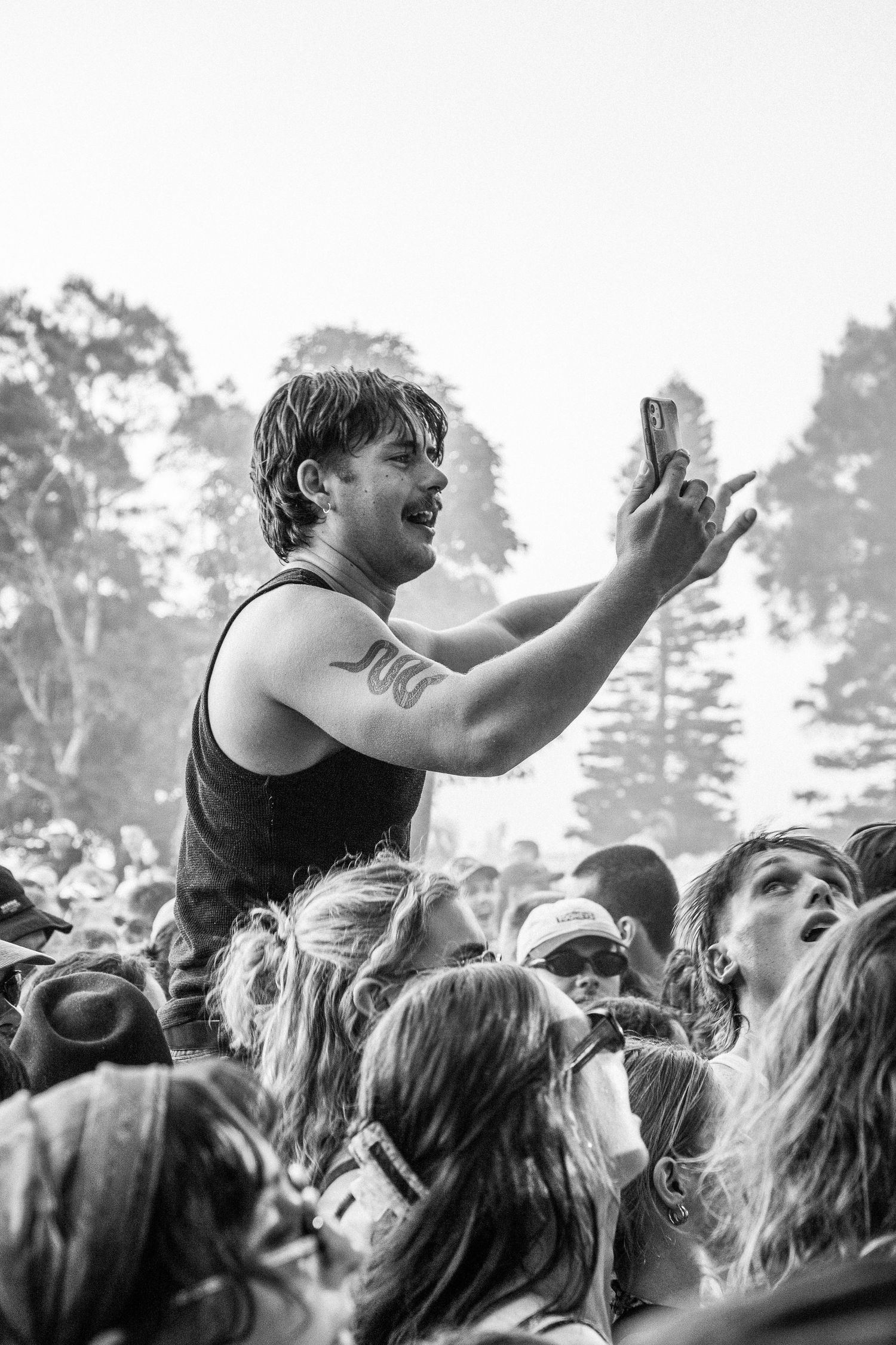 Black and white photo of excited male concert-goer on shoulders in crowd taking selfie at outdoor music Earp festival.