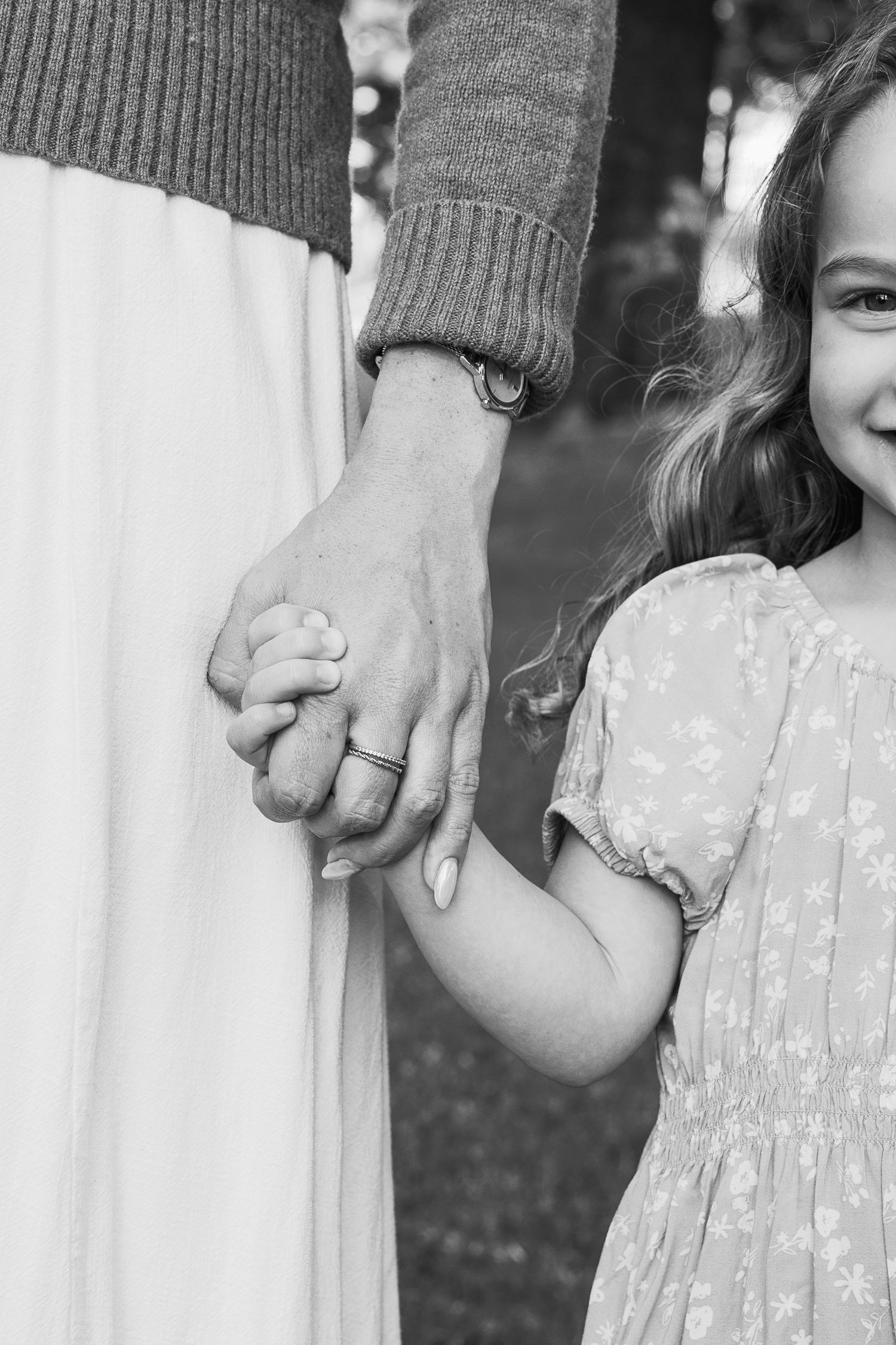 Black and white photo of a mother and young daughter holding hands outdoors, child smiling in floral dress.