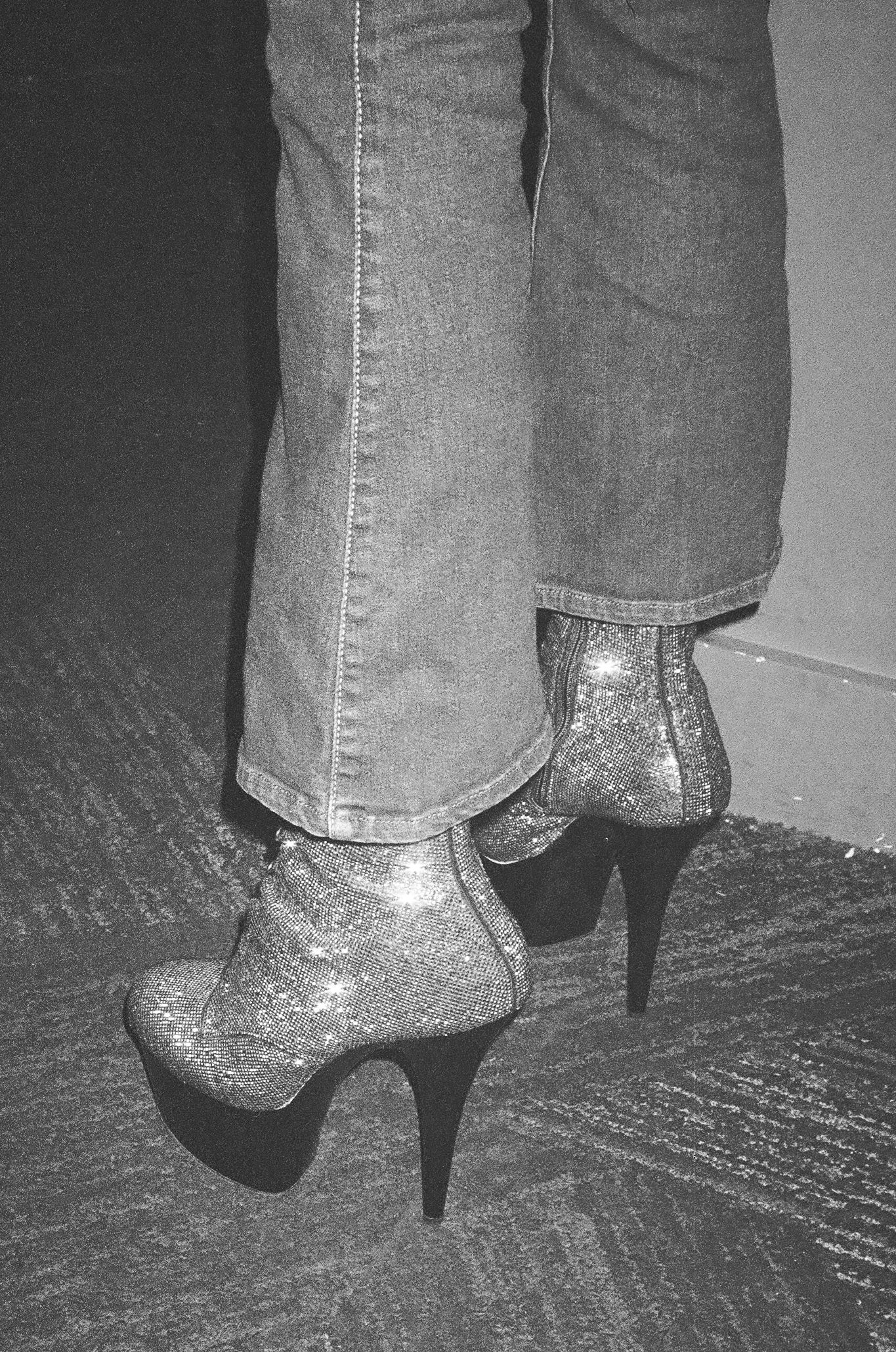 Close-up of glittery silver platform high heel ankle boots worn with flared jeans.
