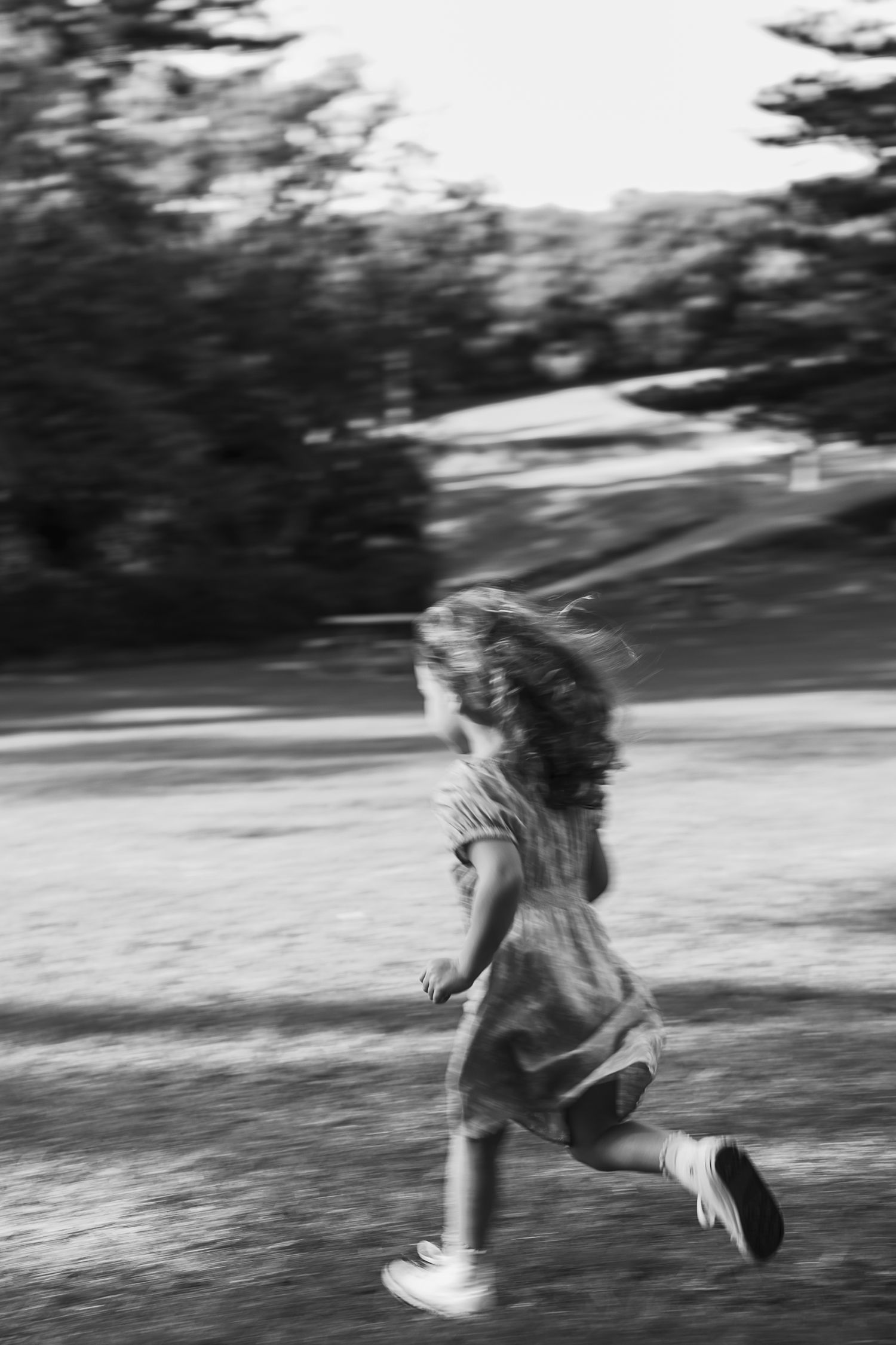 Black and white photo of a young girl with long hair running outdoors, motion blur capturing her joyful energy.