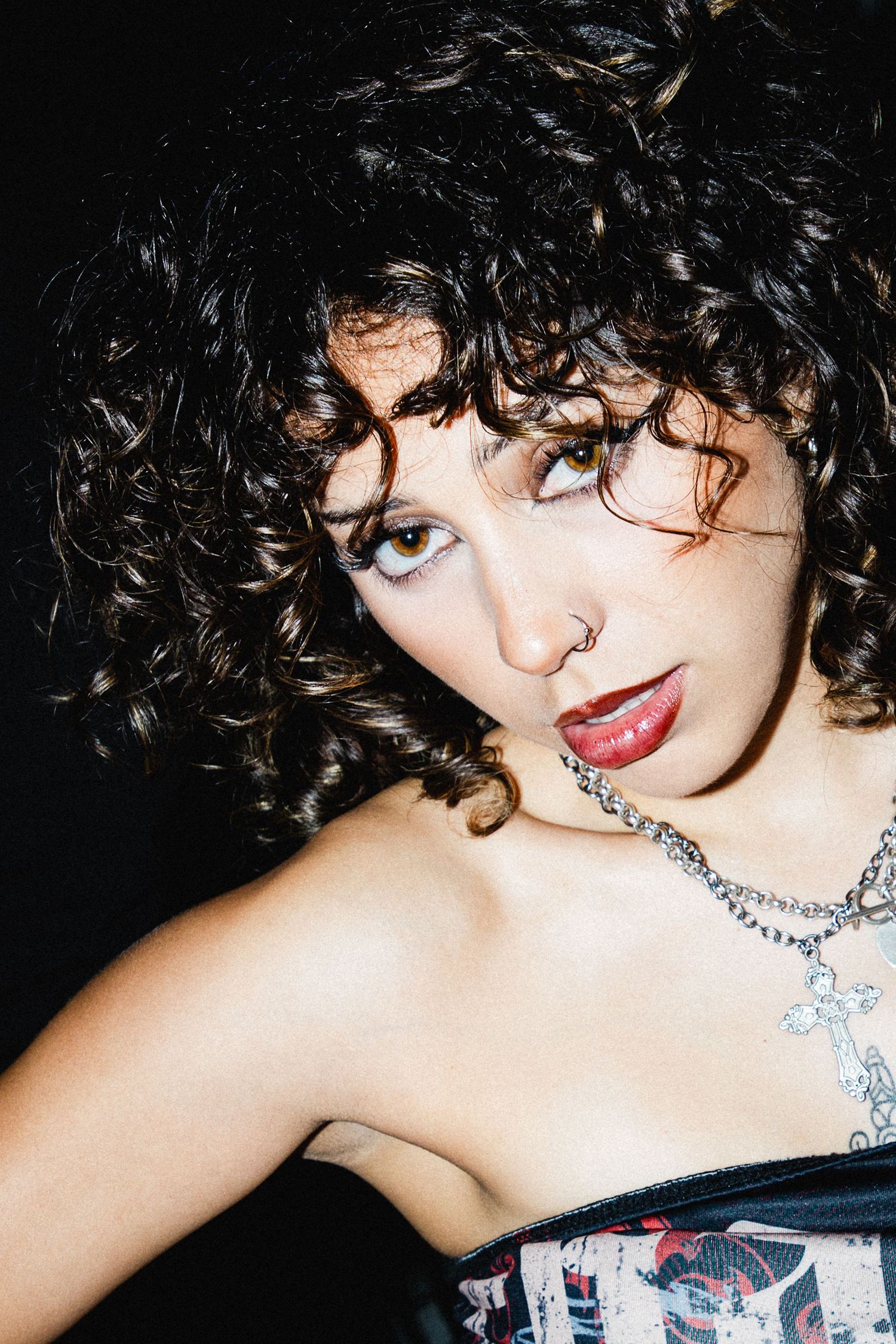 Young woman with voluminous curly dark hair, nose ring, and red lips wearing corset top and chain necklace at The Lass O'Gowrie Hotel.