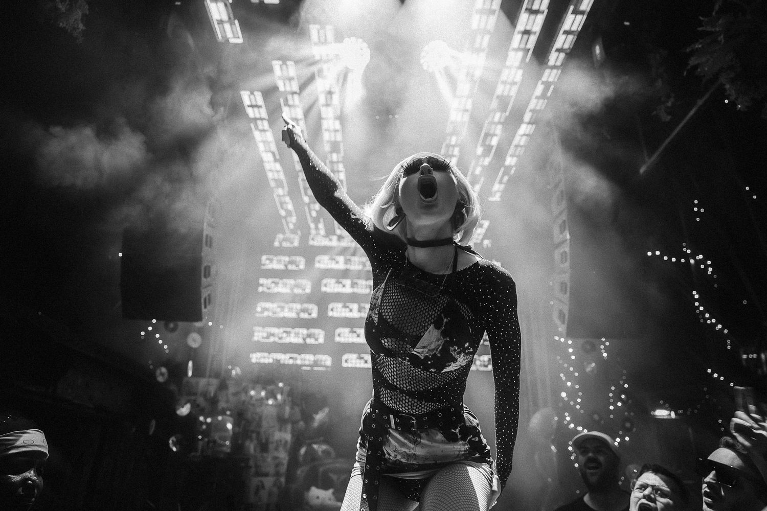 Black and white photo of a female performer raising her arm on stage at a concert with dramatic lighting.