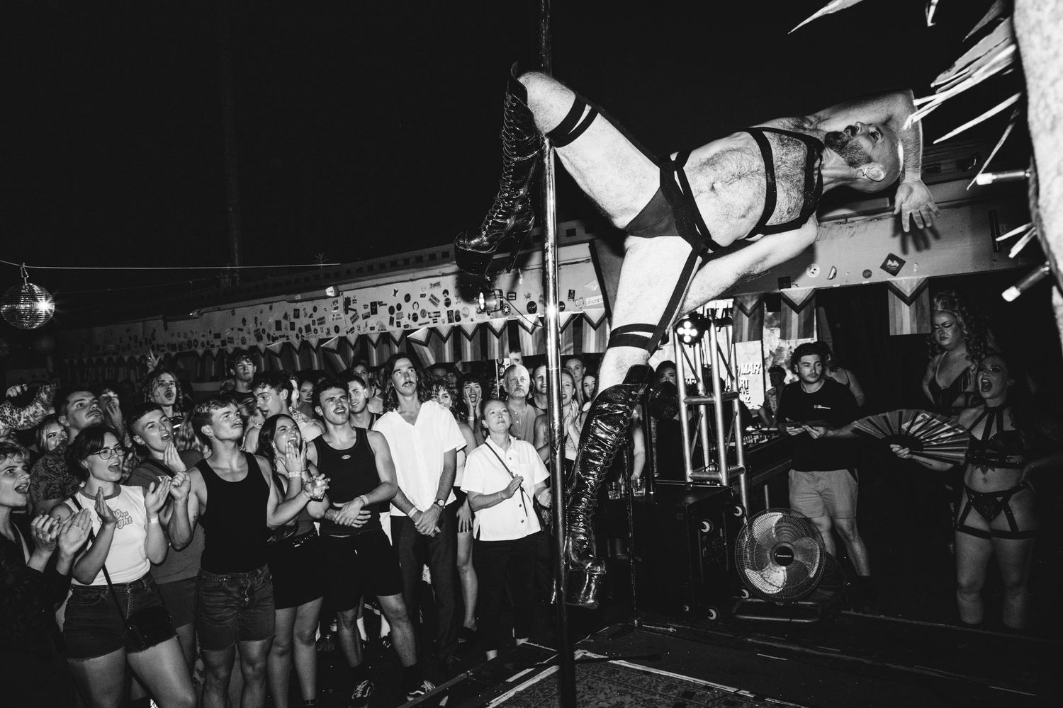 Black and white photo of a crowd watching a performer suspended in bondage gear at The Lass O'Gowrie Hotel.