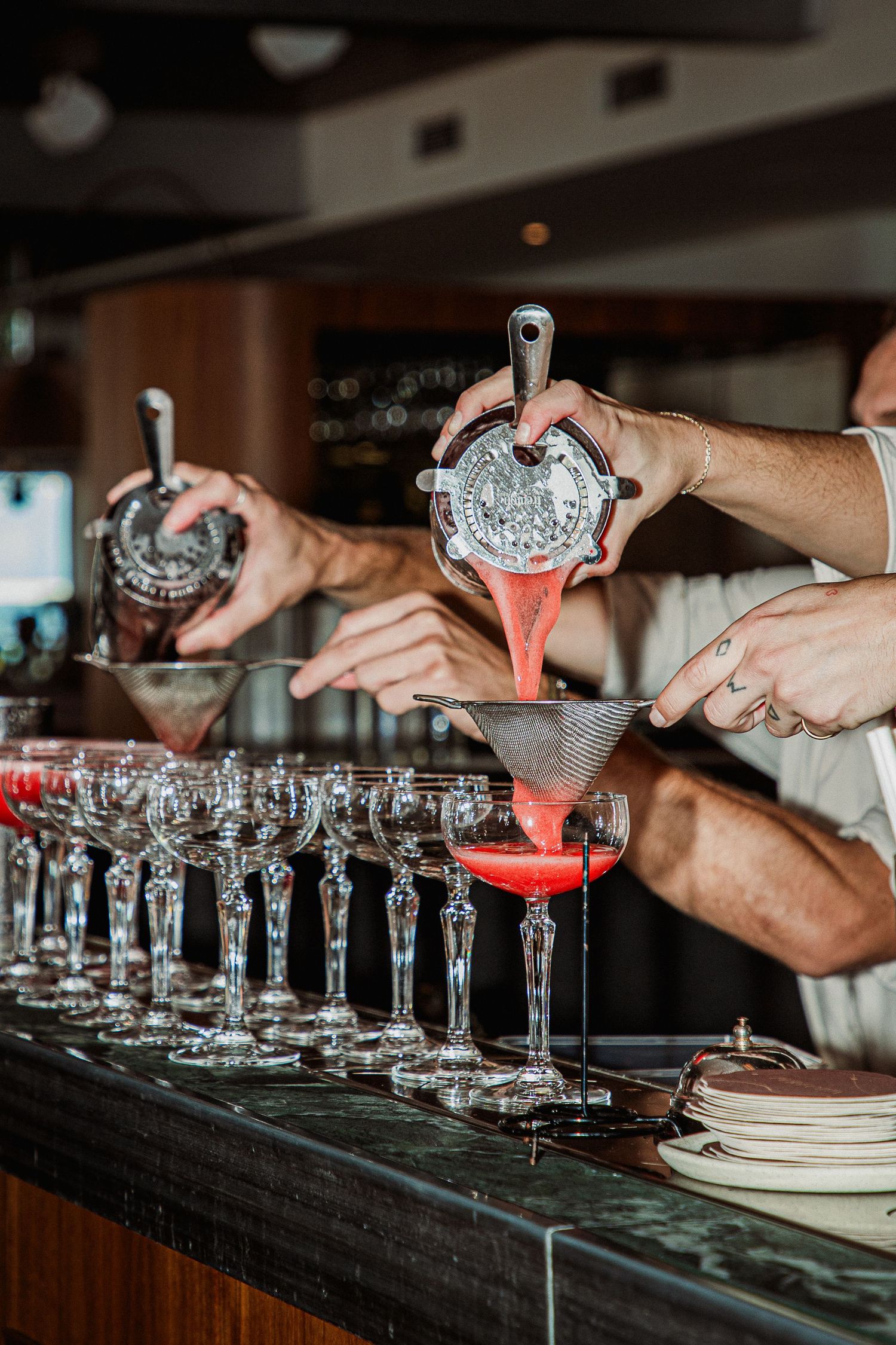 Bartenders straining red cocktails into martini glasses lined up at Peregrin Merewether.