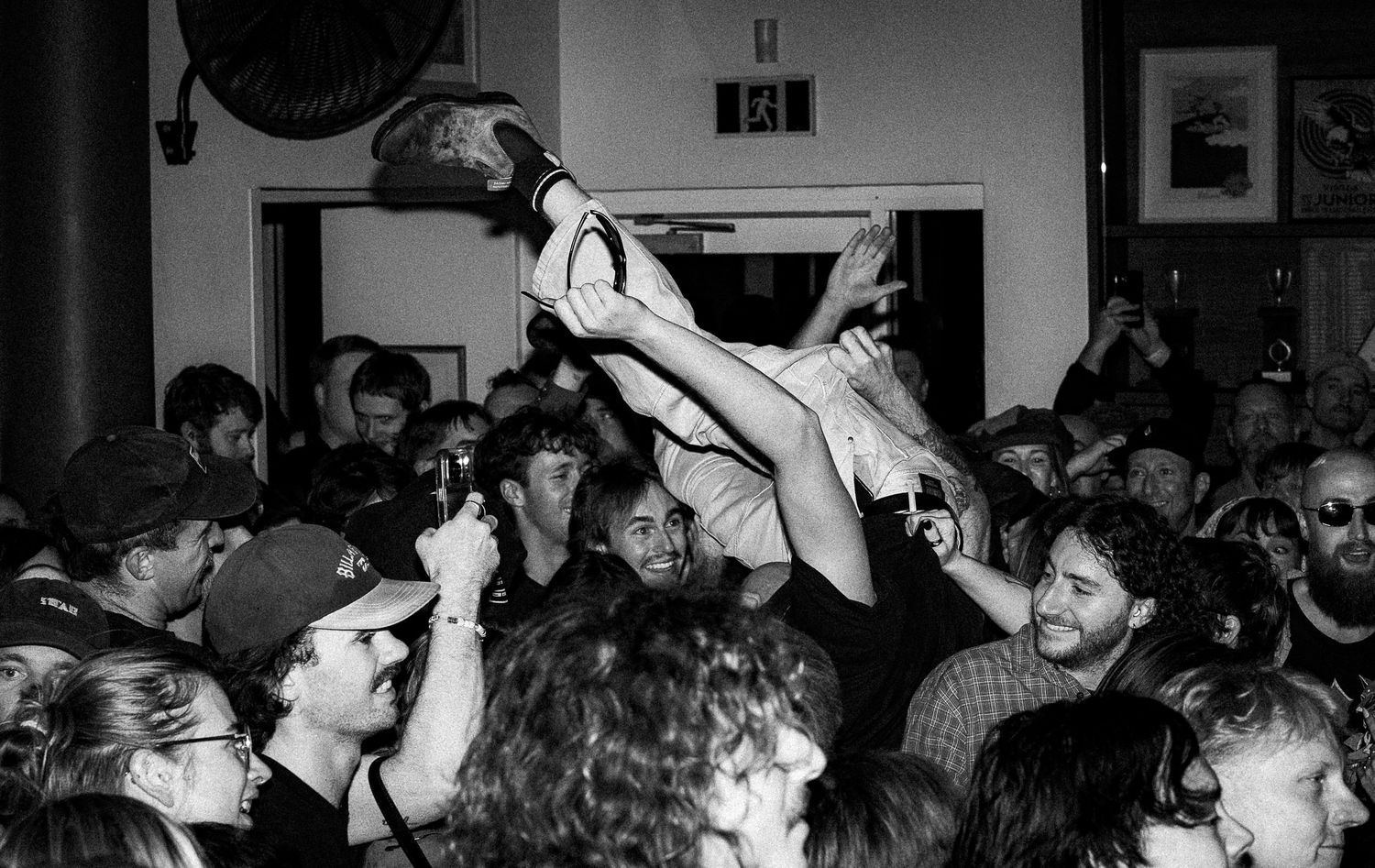 Black and white photo of a crowd surfing concert scene at a packed indoor music venue.