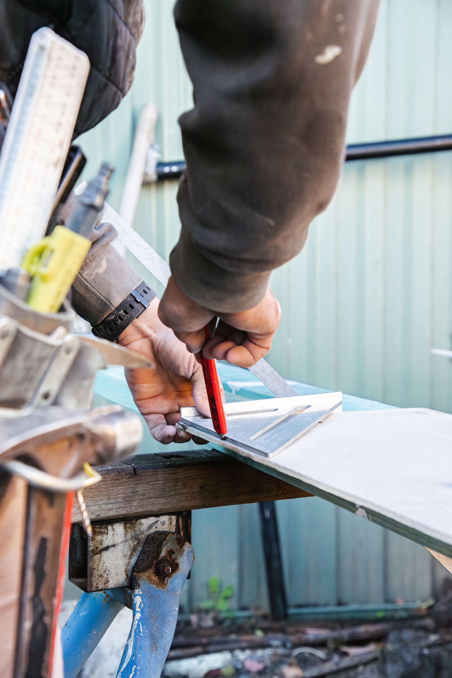 Tradesperson marking measurements on a tile with a pencil and ruler outdoors.