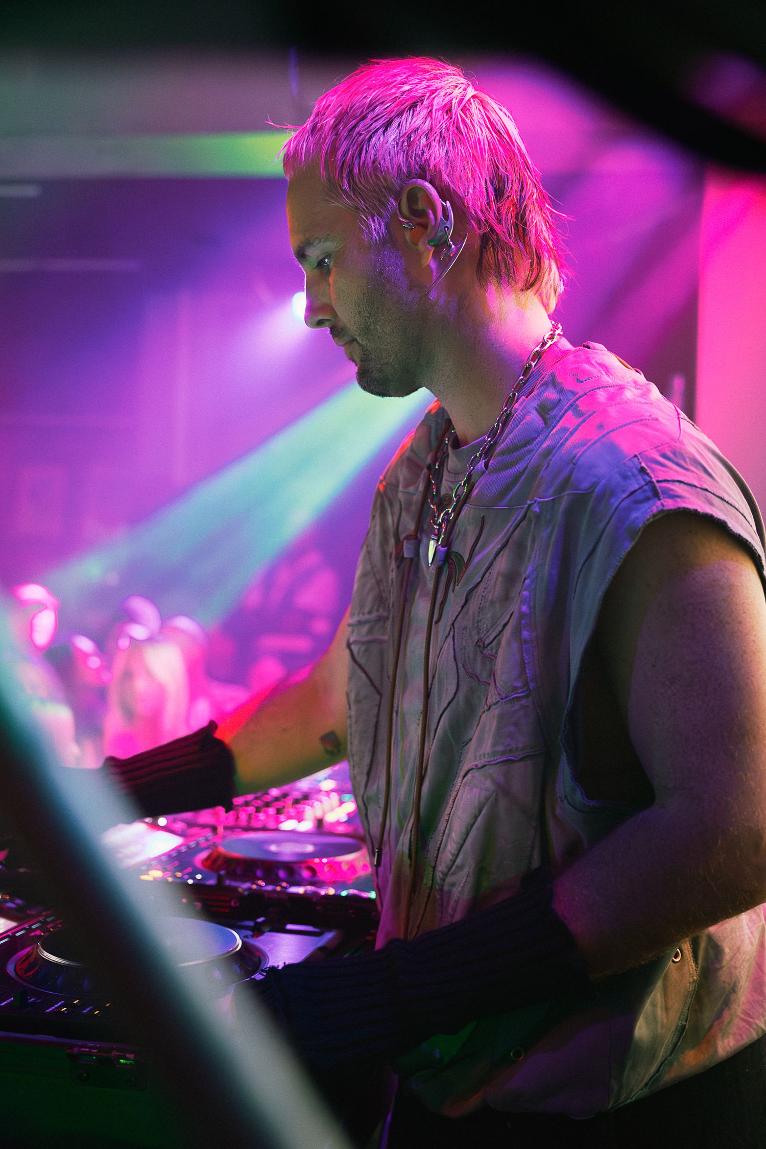 DJ performing at a nightclub under vibrant pink and purple stage lights with turntables.