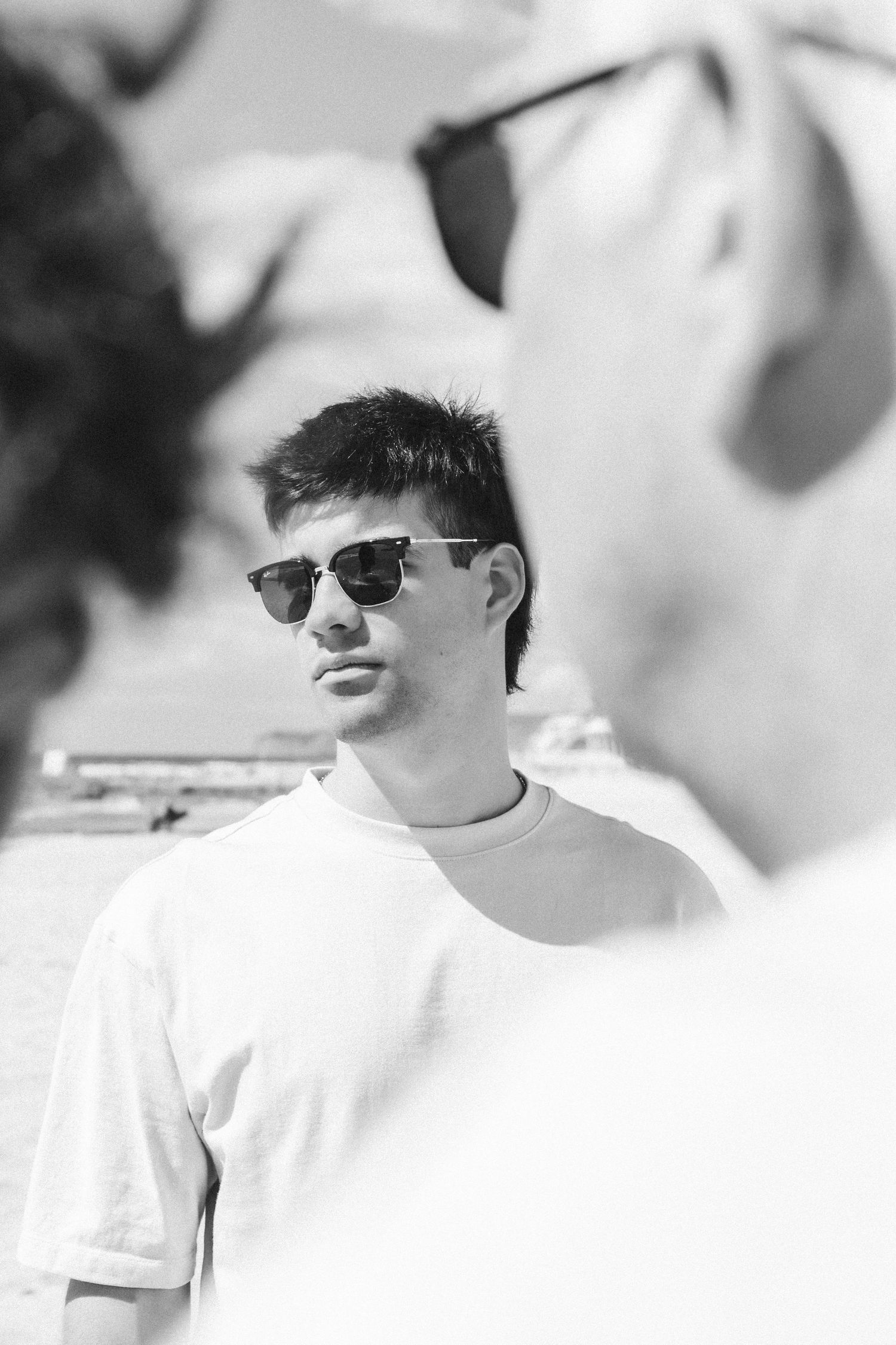 Black and white photo of a young man wearing sunglasses and a white t-shirt outdoors.