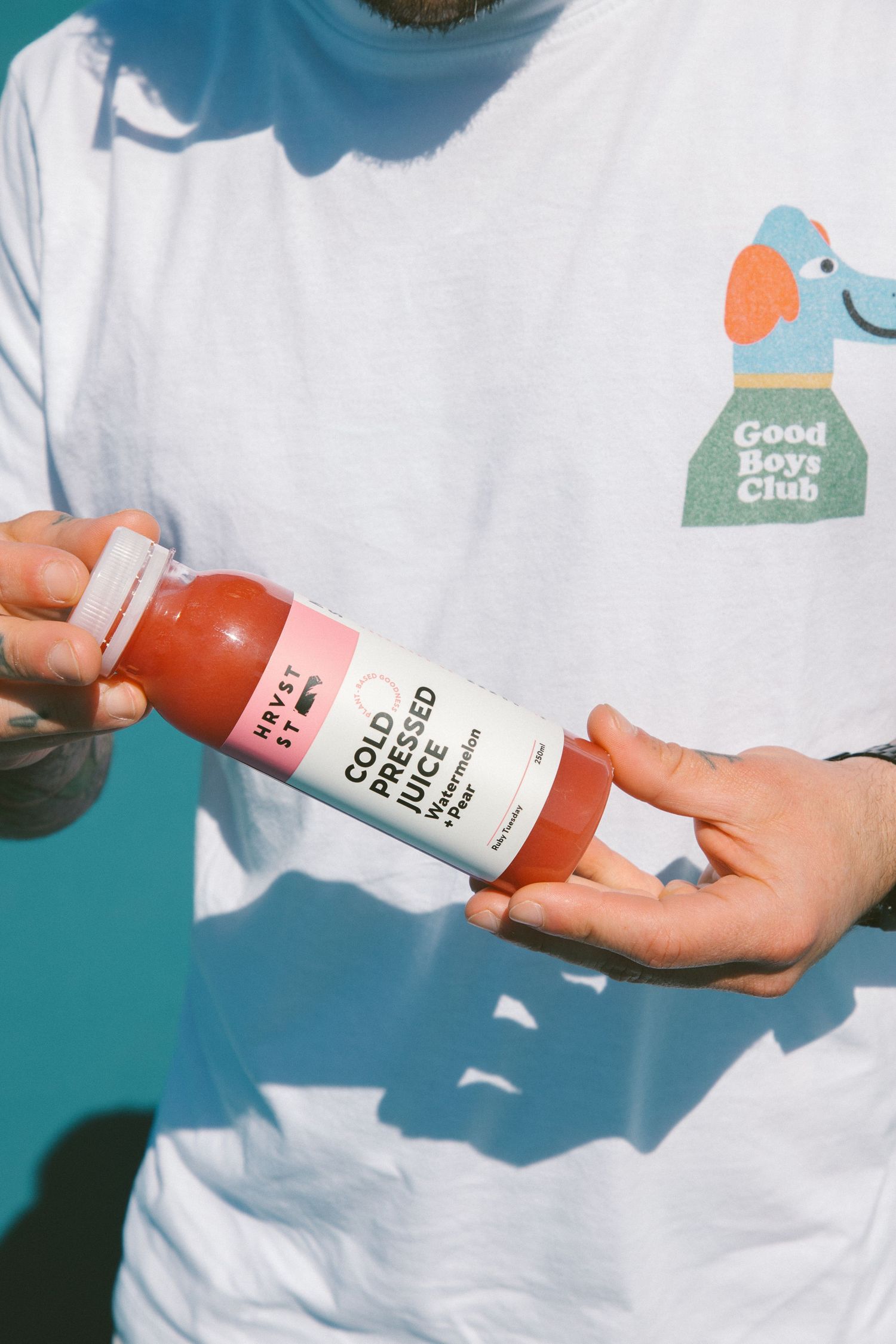 Hands holding Harvst St cold pressed watermelon juice bottle wearing Good Boys Club t-shirt.
