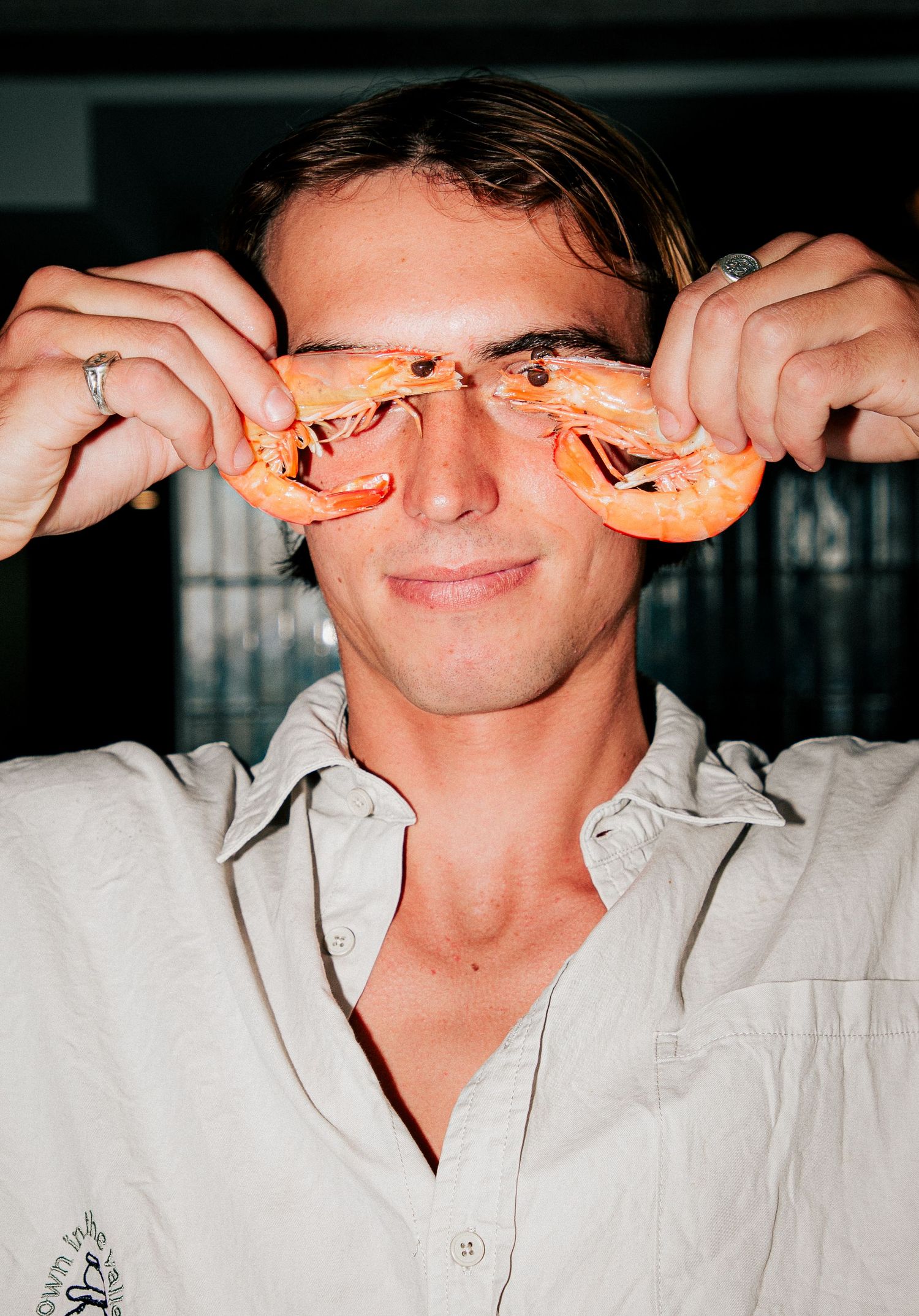 Young man holding two cooked prawns over his eyes, smiling playfully at Larrie's Takeaway Merewether.
