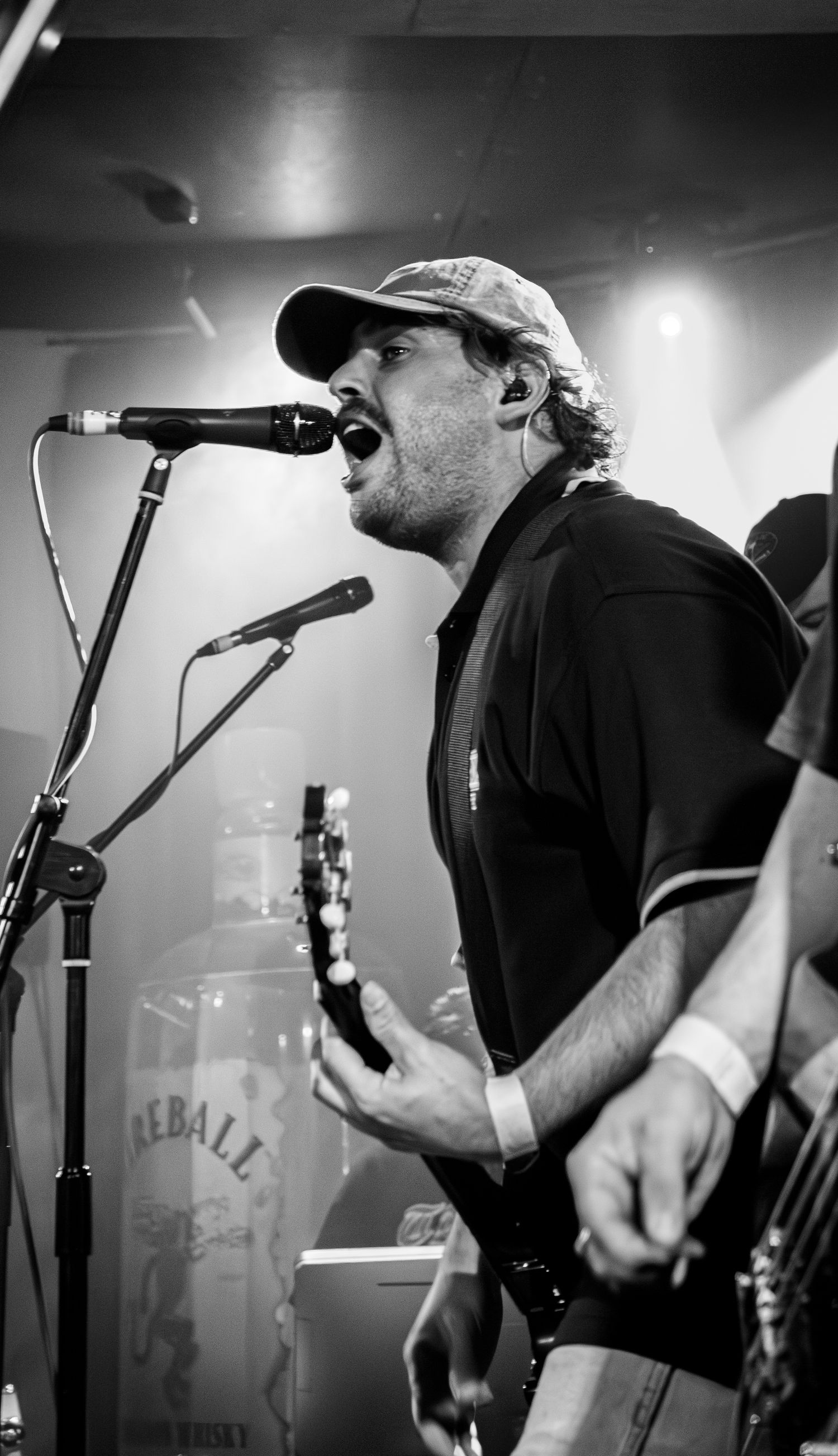 A male guitarist of Beddy Reys sings passionately into a microphone on stage in a black and white concert photo.