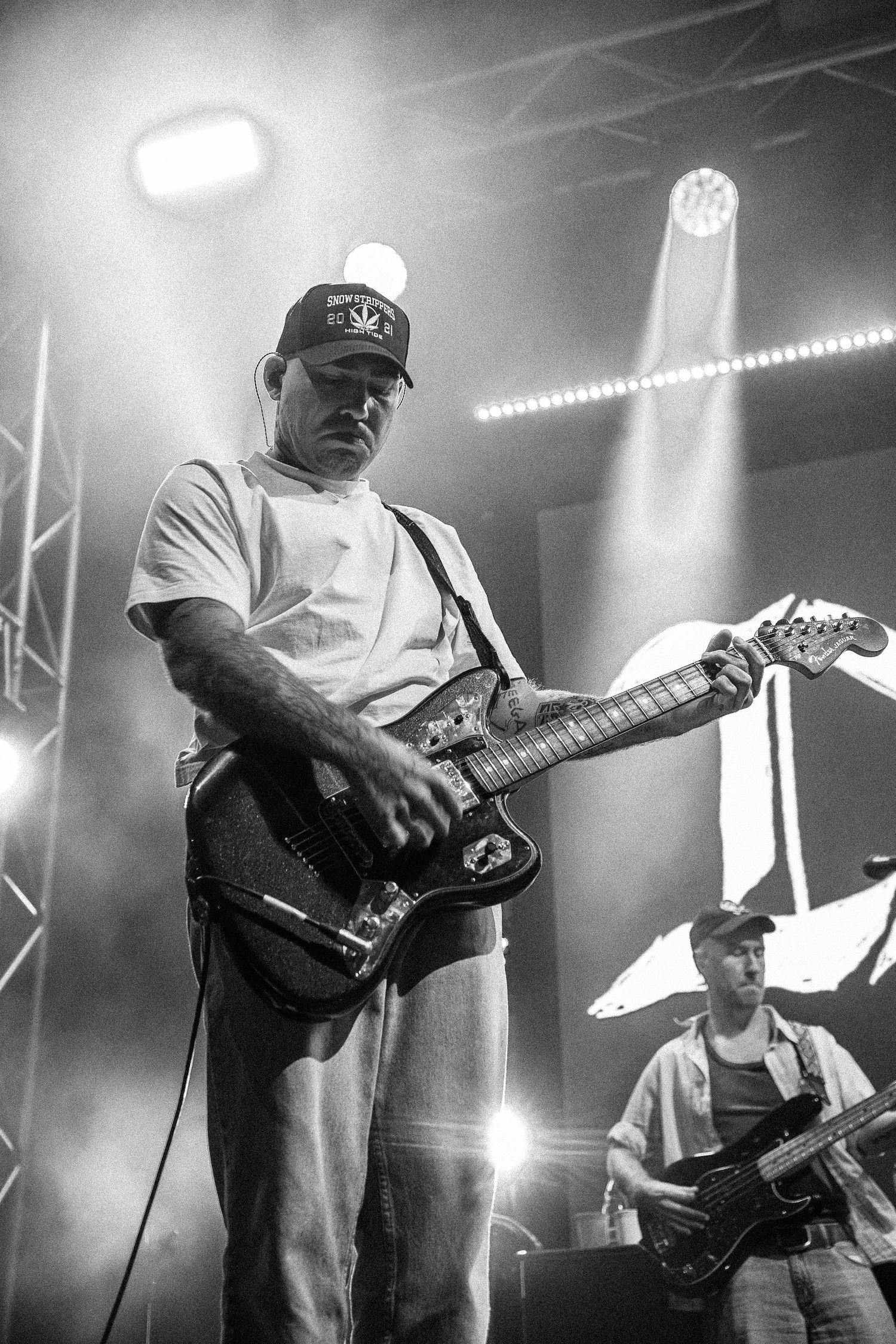 DMAs guitarist performing on stage with dramatic lighting at indoor rock concert in black and white.