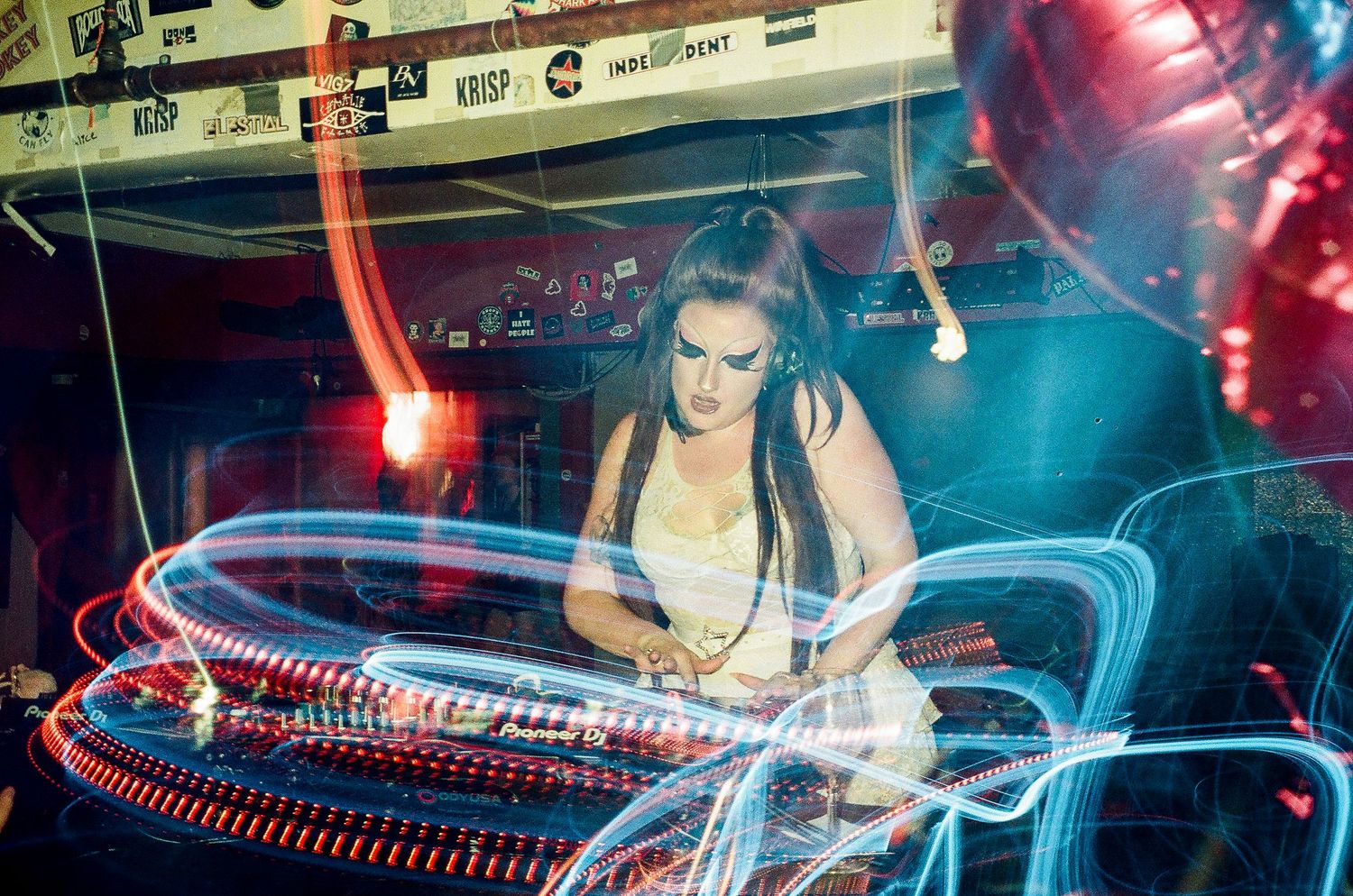 DJ performing at a nightclub with colorful light trails creating dynamic streaks across the frame The Lass O'Gowrie Hotel.