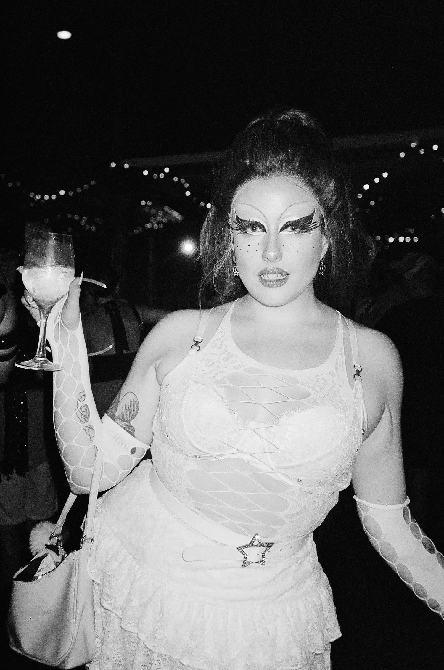 Black and white photo of a person in white lace outfit with dramatic eye makeup holding a wine glass The Lass O'Gowrie Hotel.