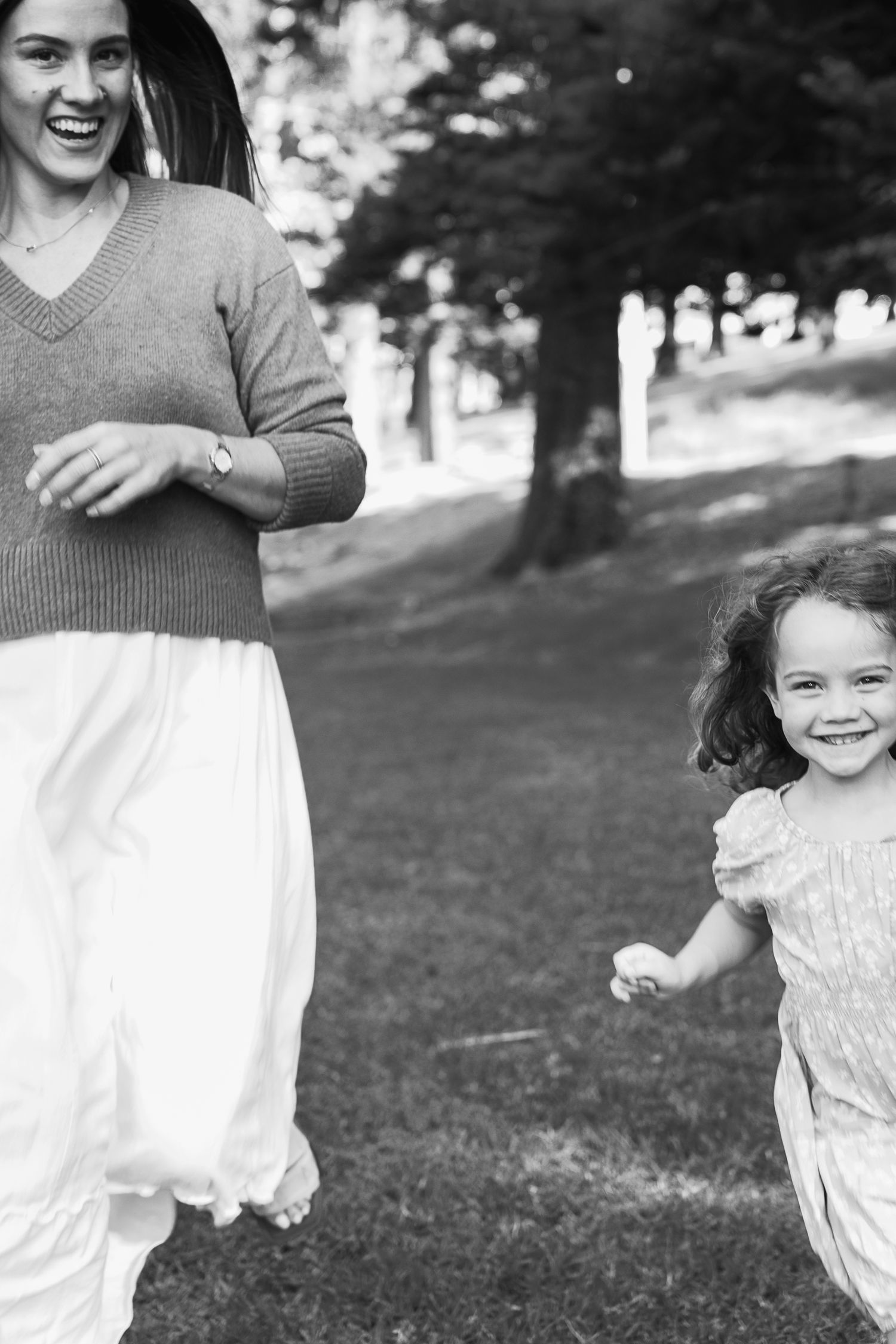 Black and white photo of a laughing mother and young daughter running together in a park.