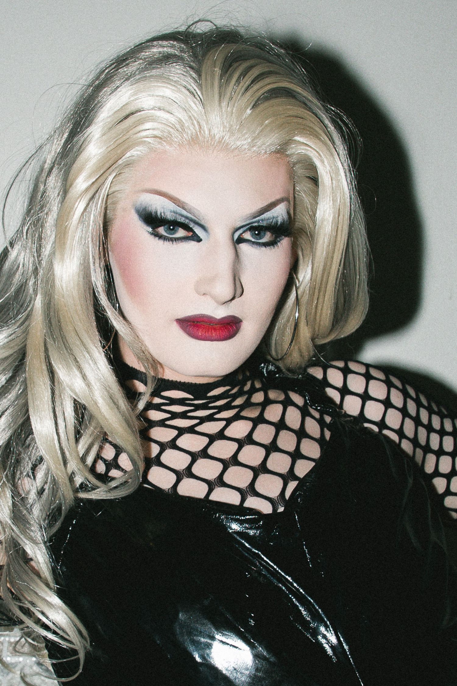 Portrait of a drag queen with platinum blonde hair, dramatic eye makeup, and black fishnet top at The Lass O'Gowrie Hotel.