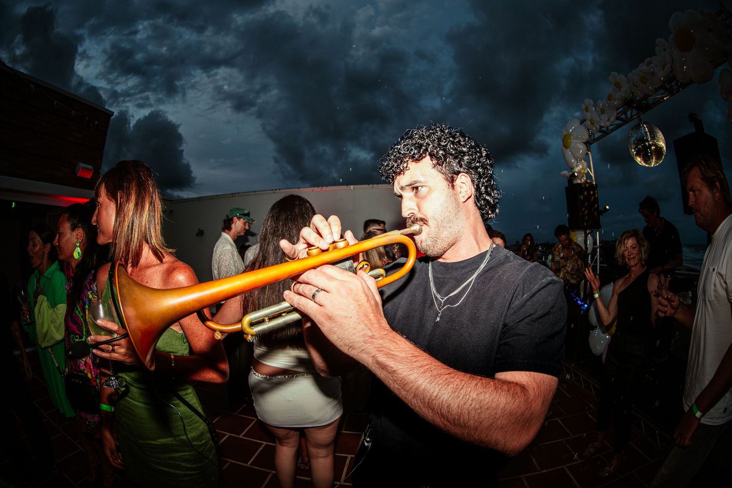 Man playing a yellow trumpet at an outdoor New Years Eve night party with crowd in background at Peregrin Merewether.