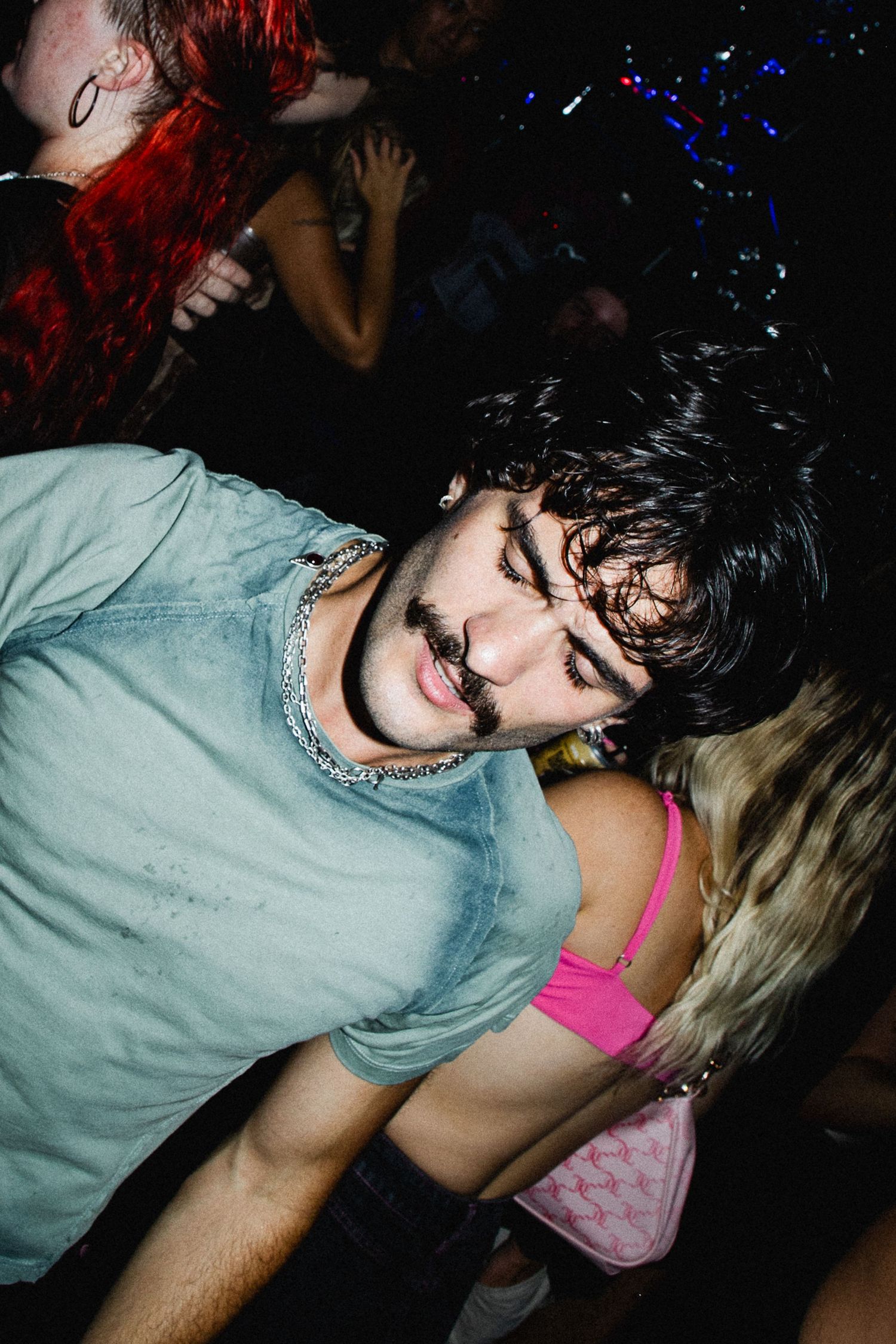 Young man with dark curly hair in denim shirt dancing at nightclub party.