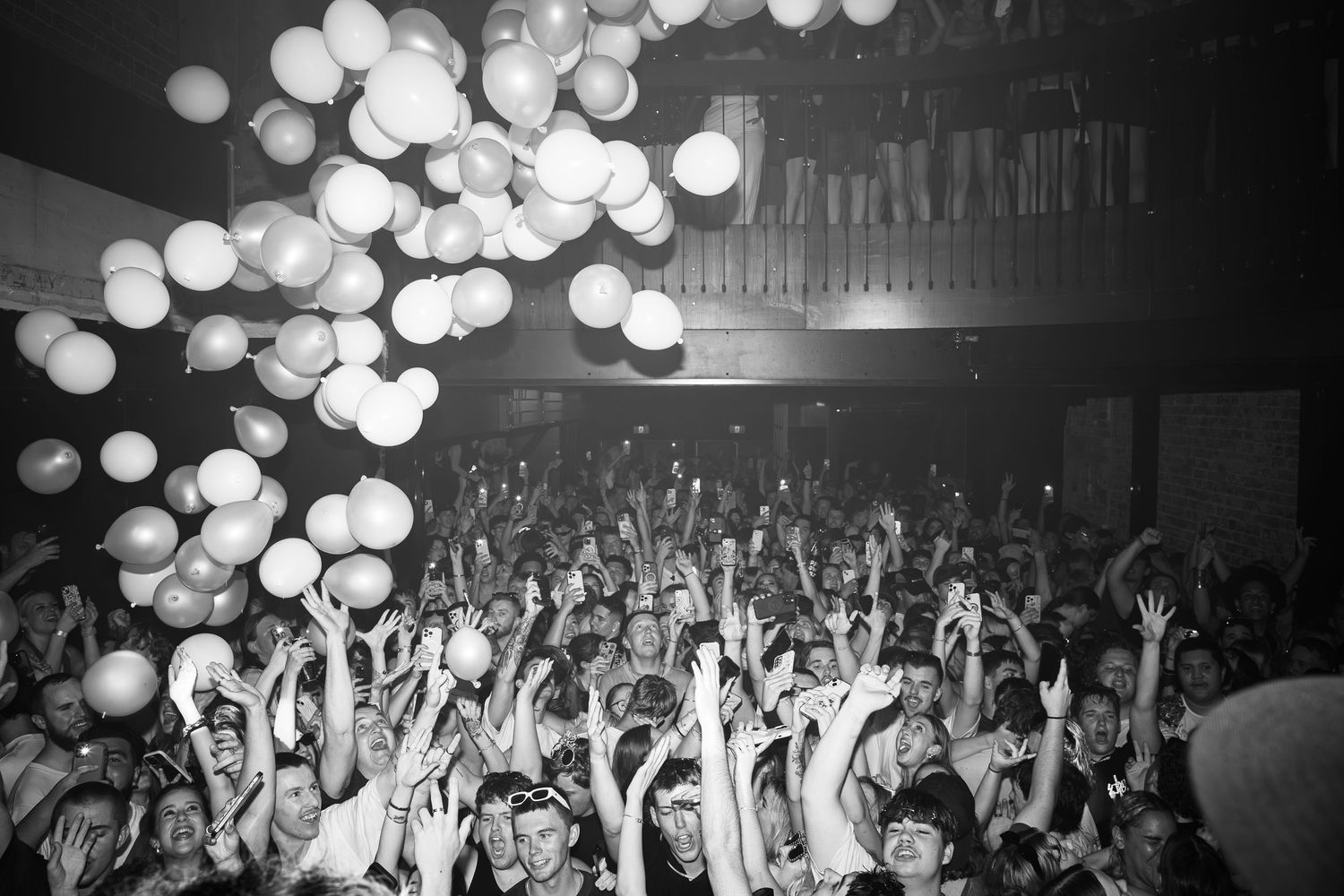 A crowd of concert-goers reach up to touch balloons falling from the ceiling at a New Years Eve event at King Street Hotel Newcastle.