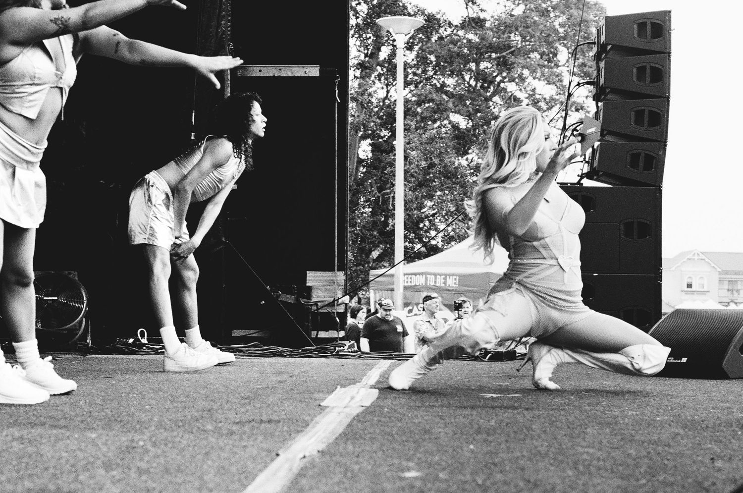 Black and white photo of performers dancing on outdoor stage at Newcastle Pride Fair Day.