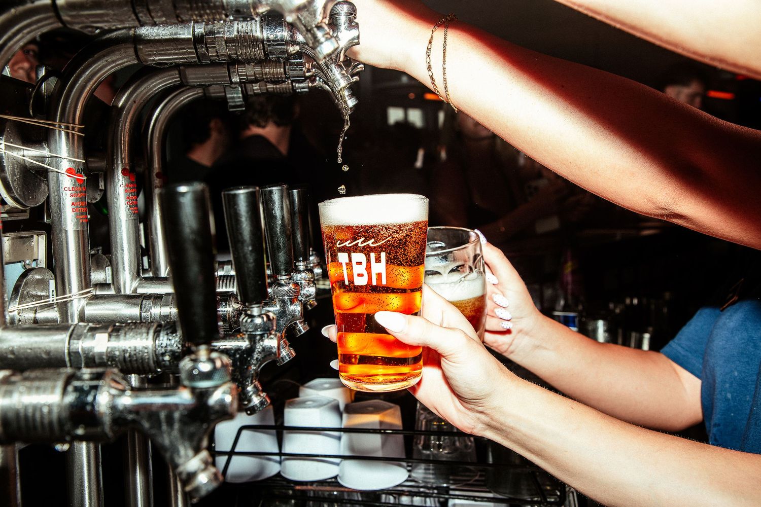Bartender pouring draft beer into a branded pint glass from tap.