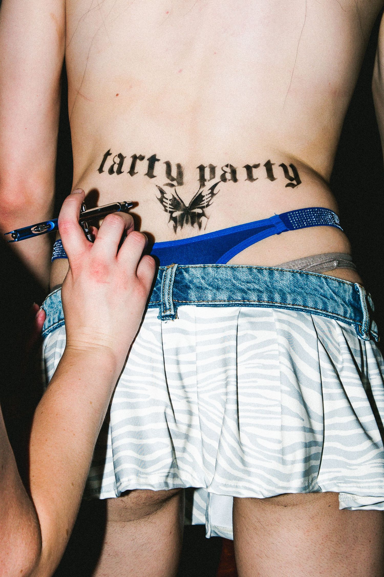 Close-up of a lower back tattoo reading tarty party with a bird design being drawn on at The Lass O'Gowrie Hotel.