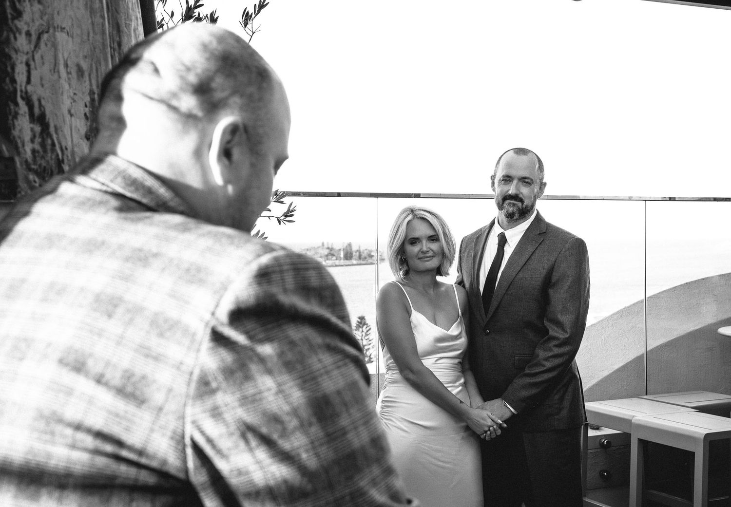 Black and white photo of couple exchanging vows before officiant during intimate outdoor wedding ceremony.
