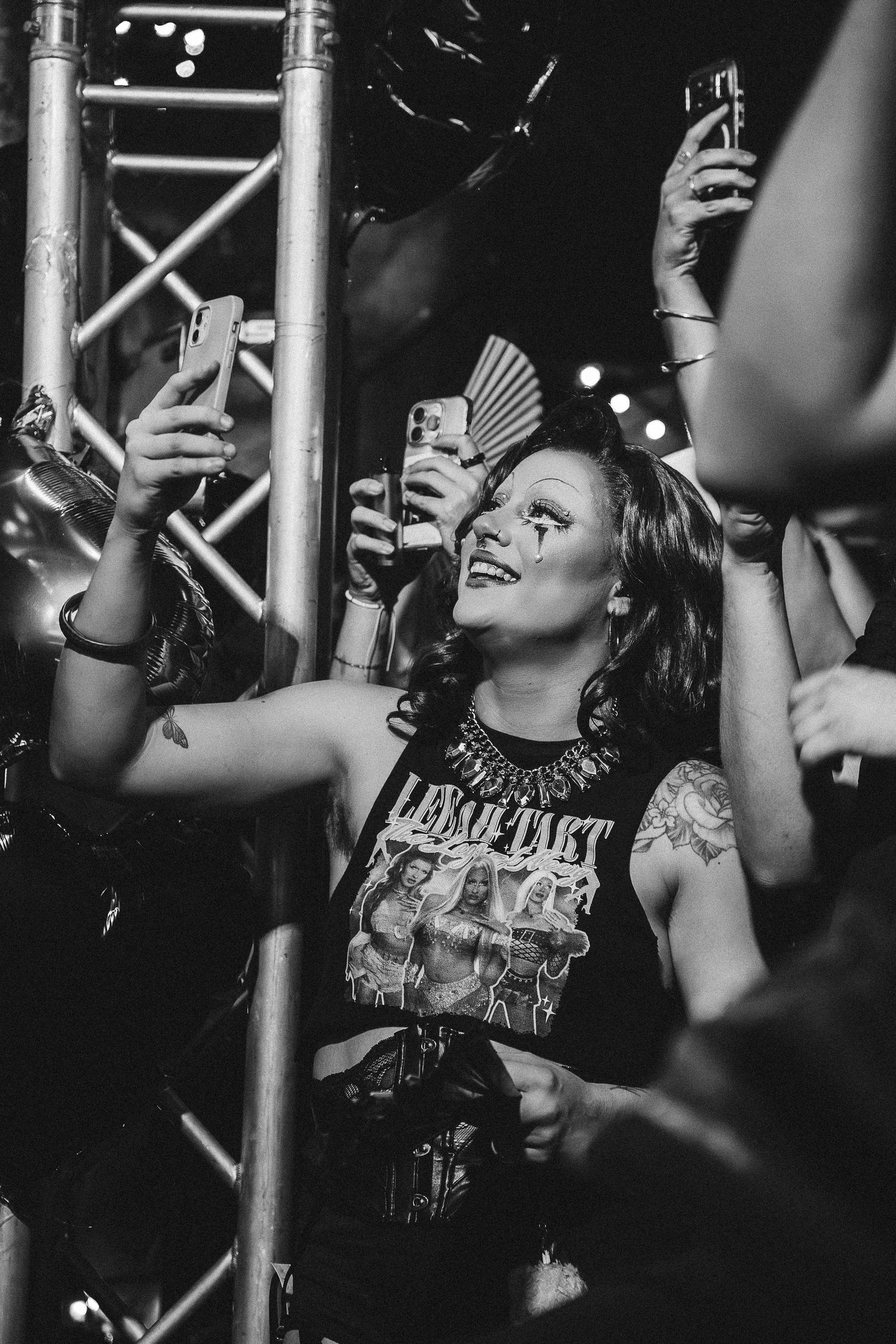 Person in crowd in band tee smiling and taking selfie at crowded concert venue event at The Lass O'Gowrie Hotel.