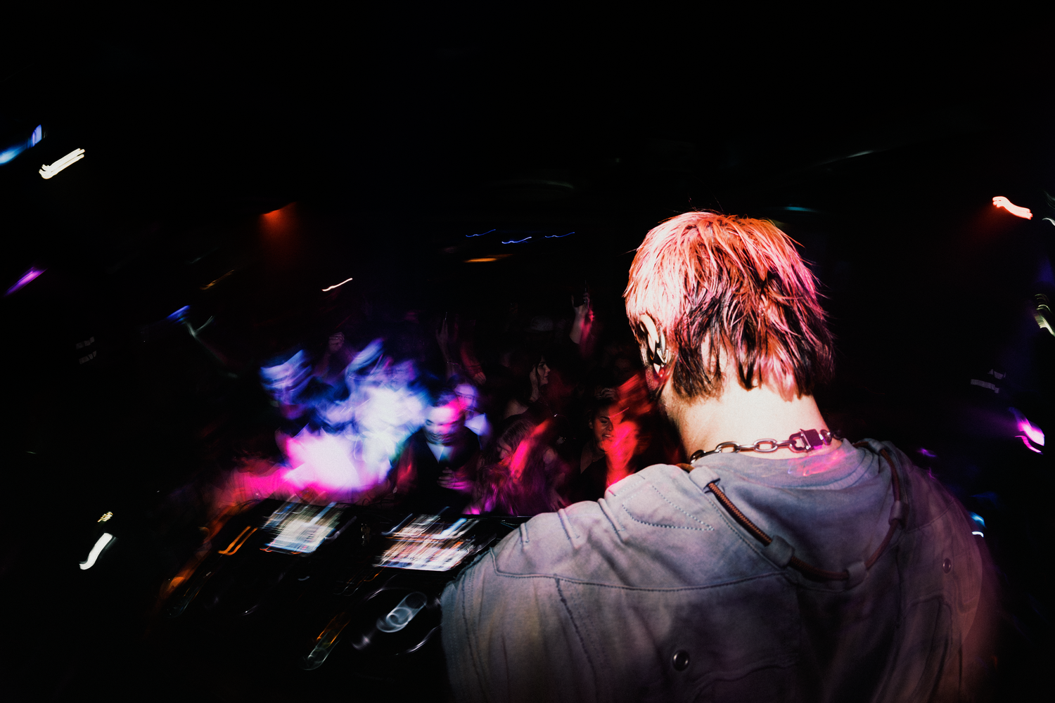 DJ performing at a nightclub with colorful lights and crowd in the background.
