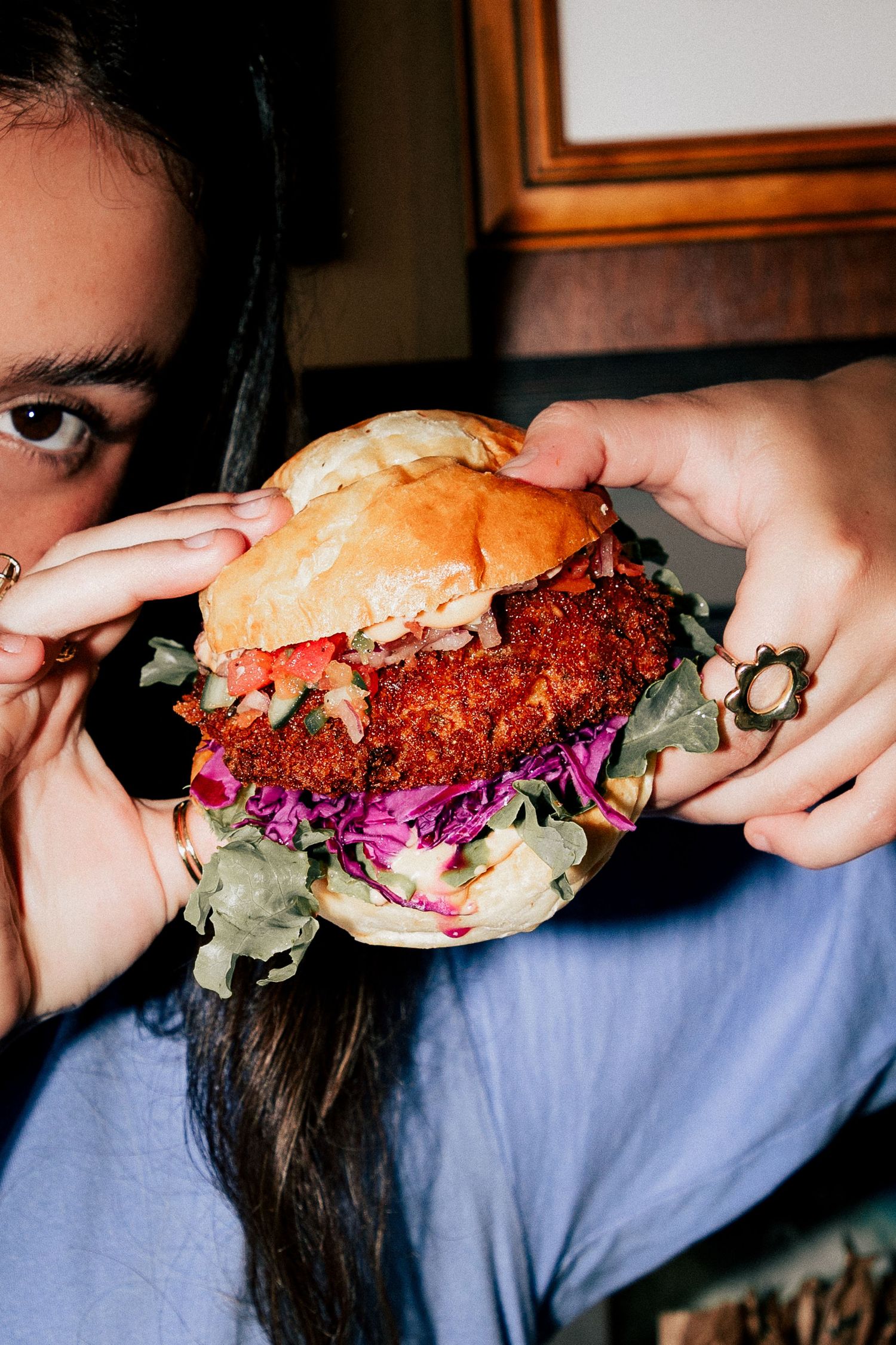 Person holding a large crispy fried chicken burger with purple cabbage and lettuce close to their face at Larrie's Takeaway Merewether.