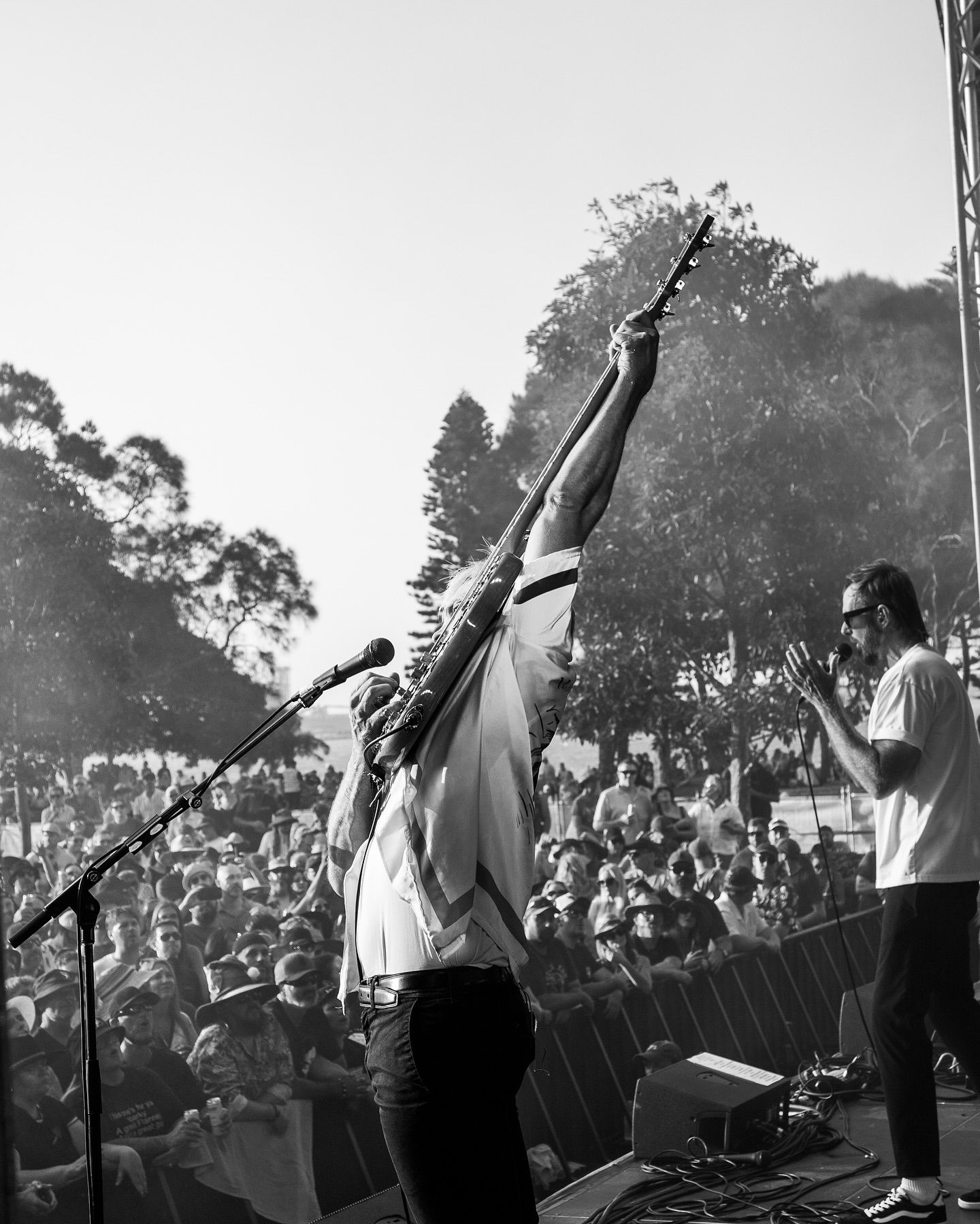 Guitarist from Birds of Tokyo raises guitar triumphantly above head on outdoor stage before large crowd.