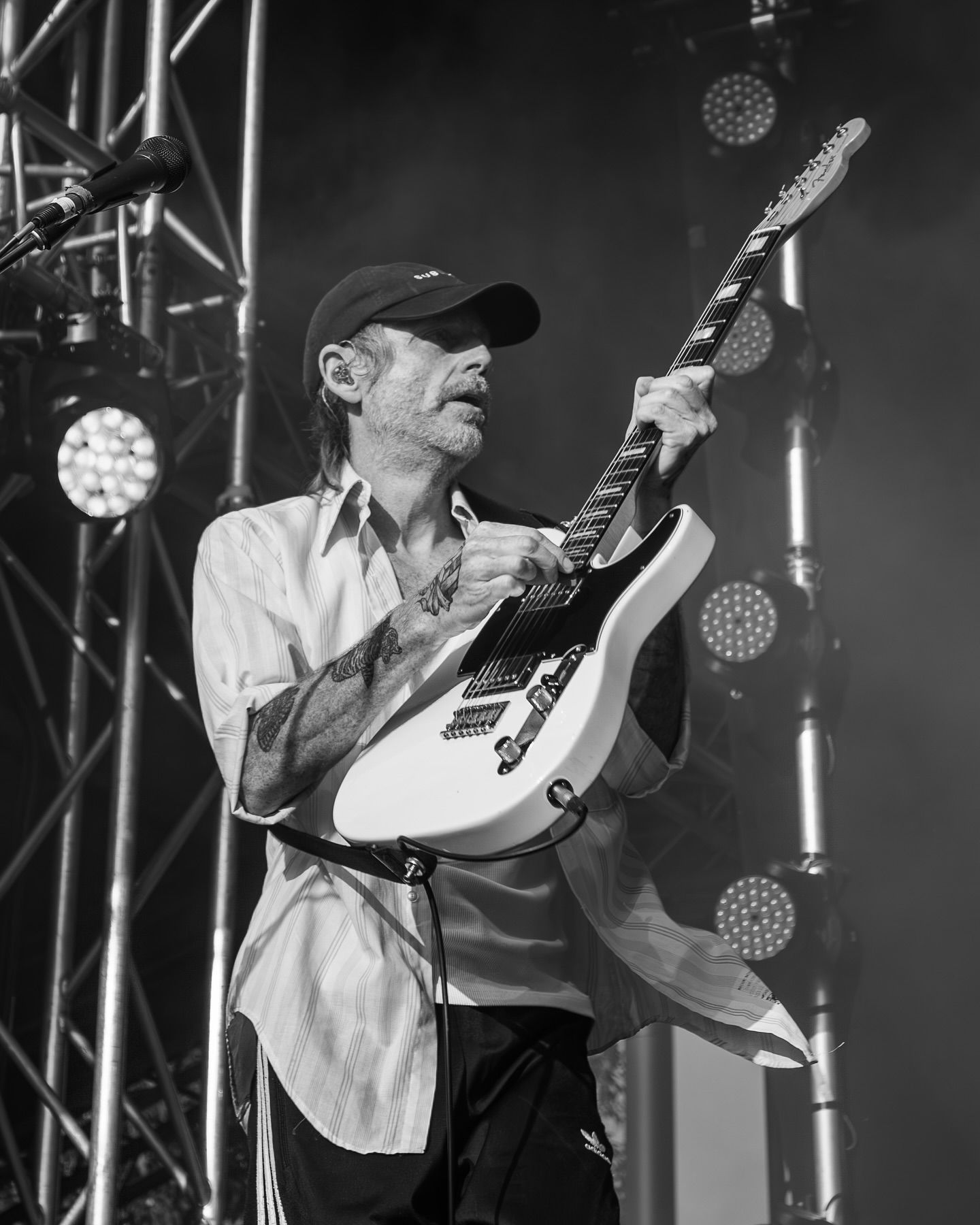 Guitarist from Birds of Tokyo plays white electric guitar on stage wearing cap under concert stage lights.