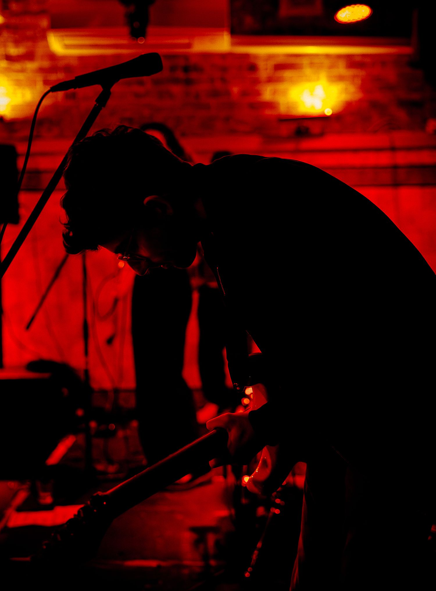 Silhouetted musician performing on stage bathed in dramatic red lighting at a live music venue.