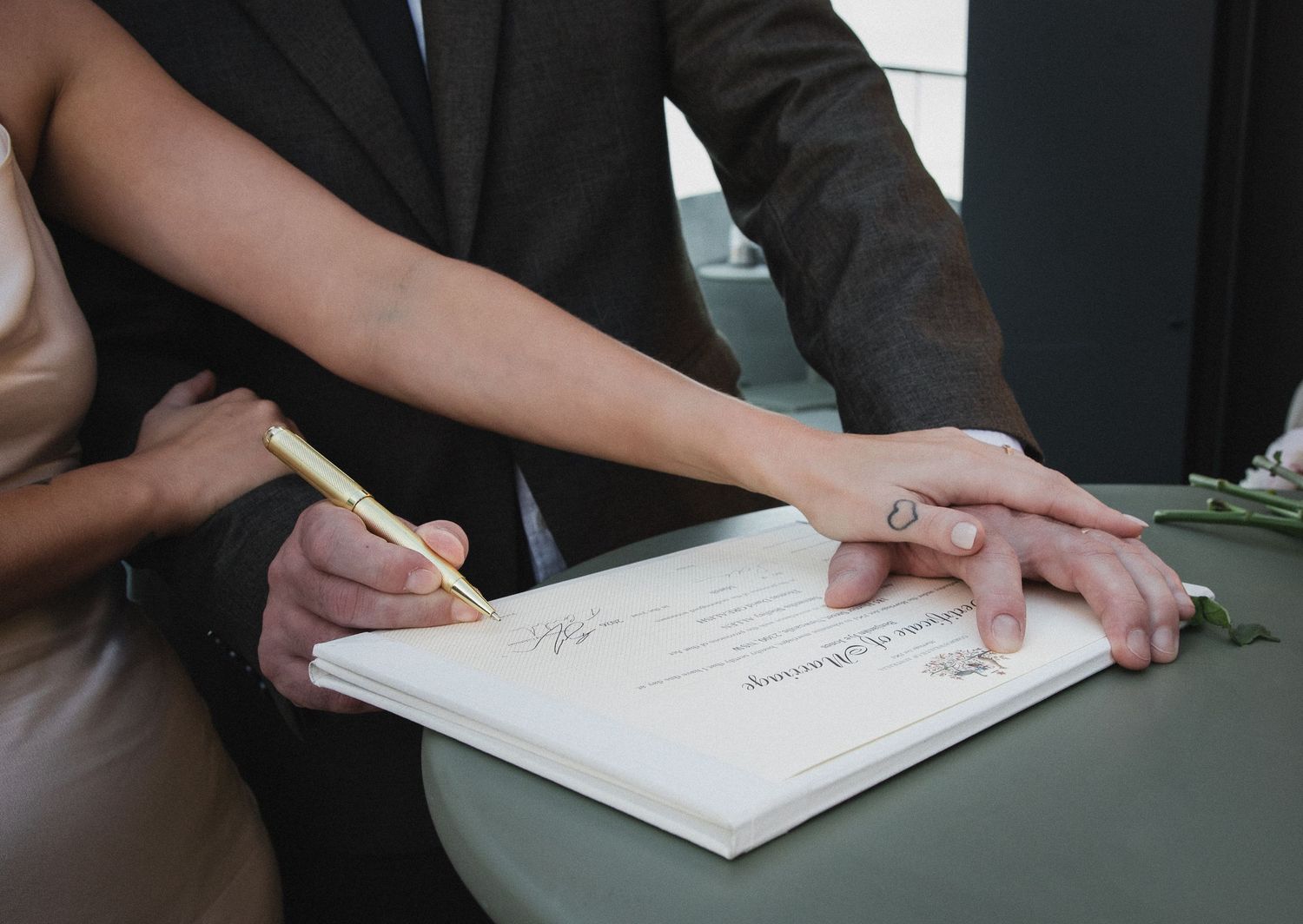 Couple signing wedding marriage certificate document with gold pen during intimate elopement ceremony.