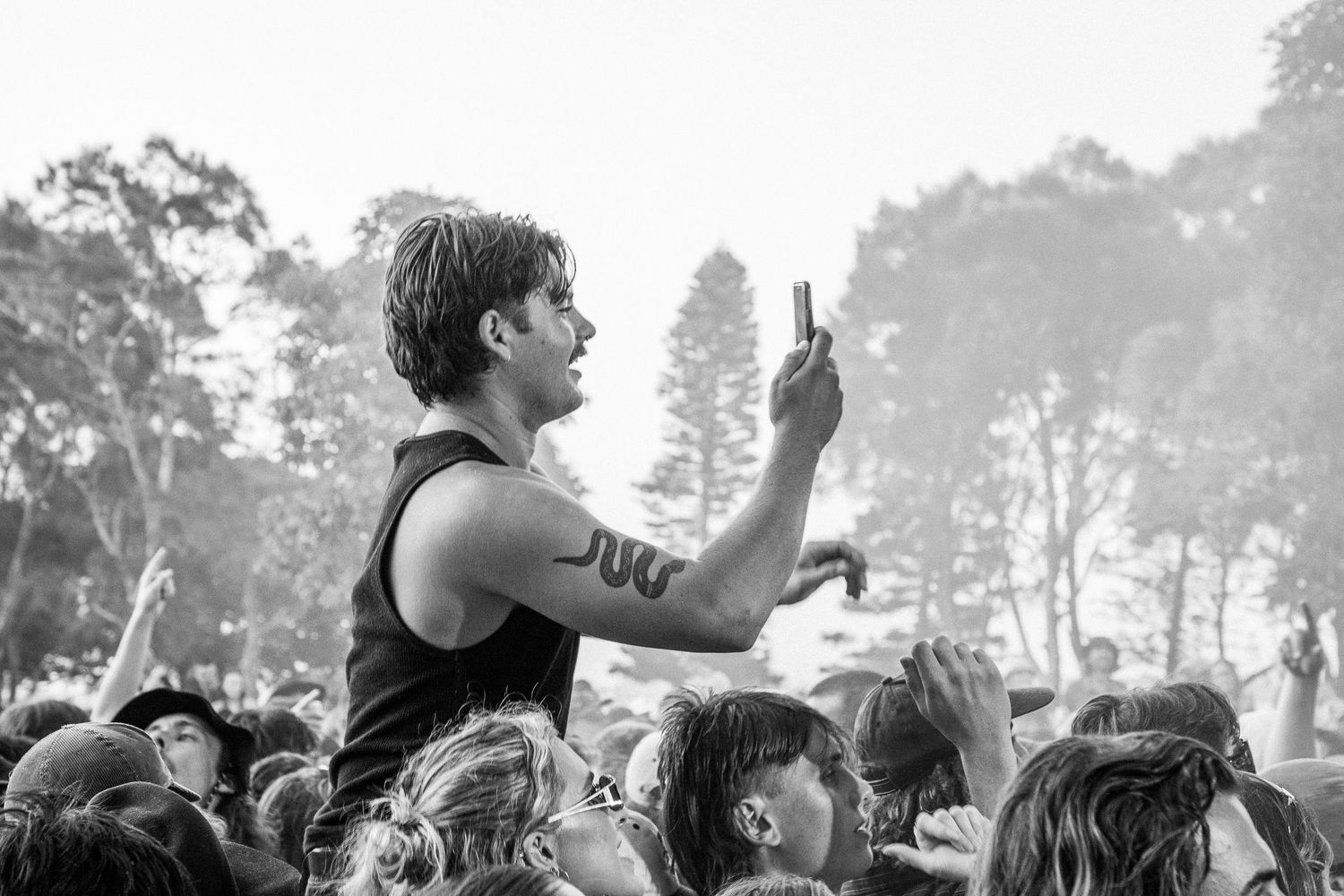 Black and white photo of a man holding a phone aloft in a crowded outdoor Earp music festival.