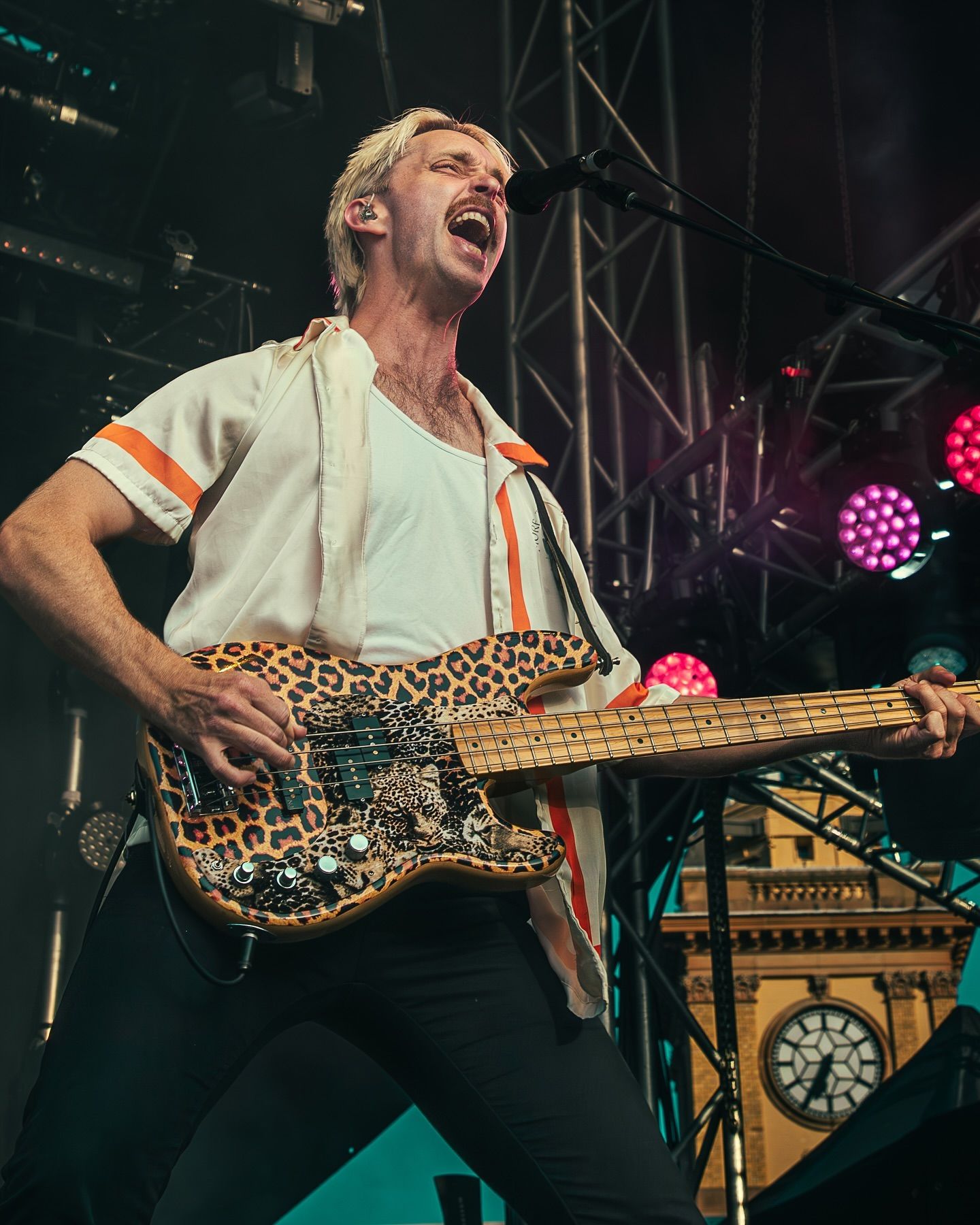Guitarist from Birds of Tokyo performs on stage with leopard print electric guitar under colorful concert lights.