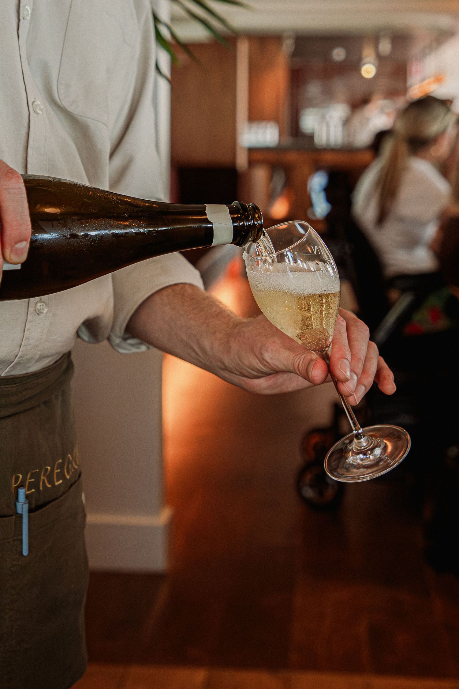 Waiter pouring champagne into a wine glass at Peregrin Merewether.