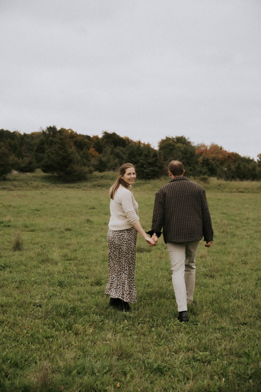 Paar läuft Hand in Hand über eine herbstliche Wiese von hinten