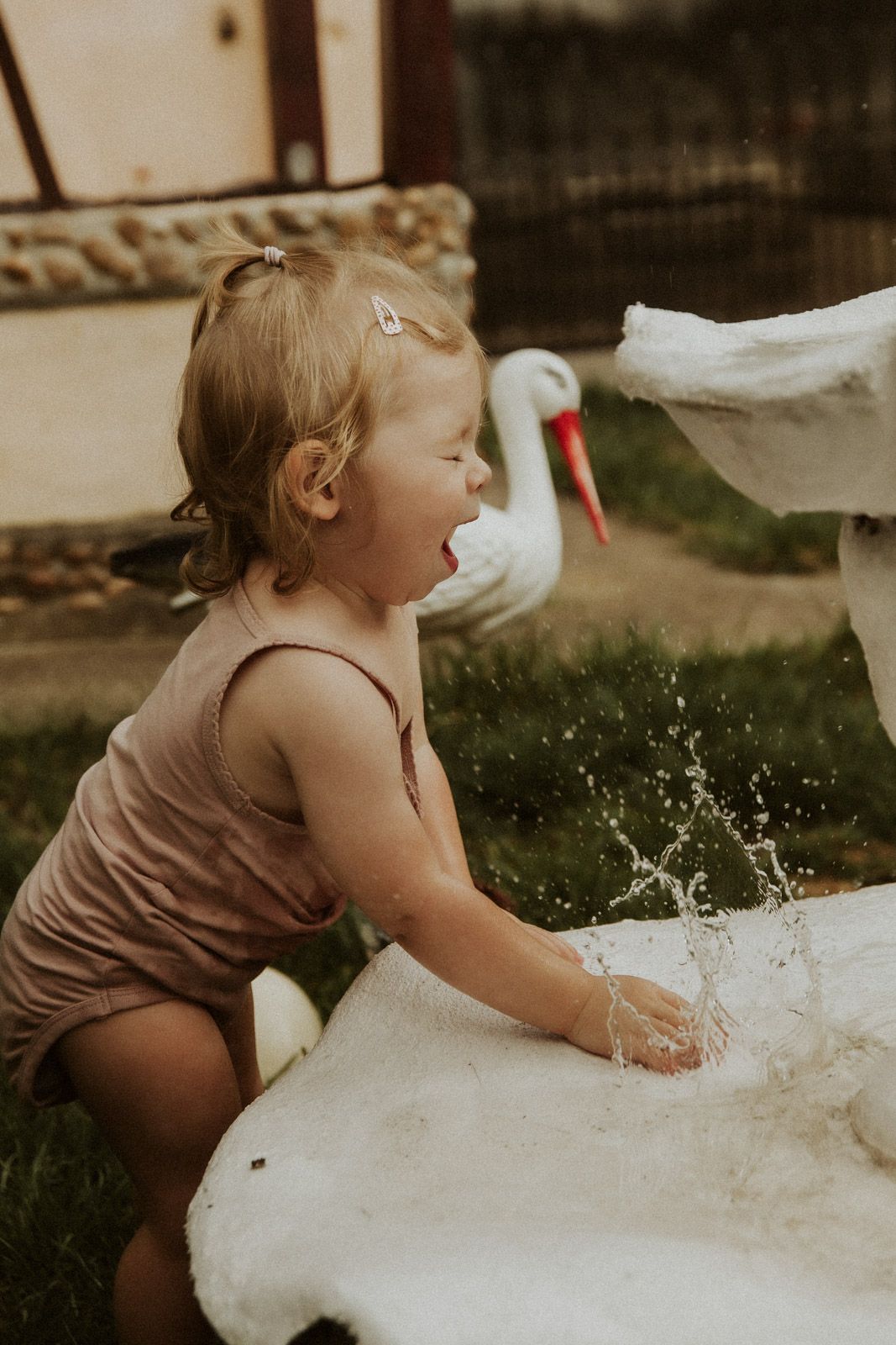 Kleinkind lacht ausgelassen beim Planschen in einer Wasserschale mit Storch – Kinderfotografie Ingolstadt