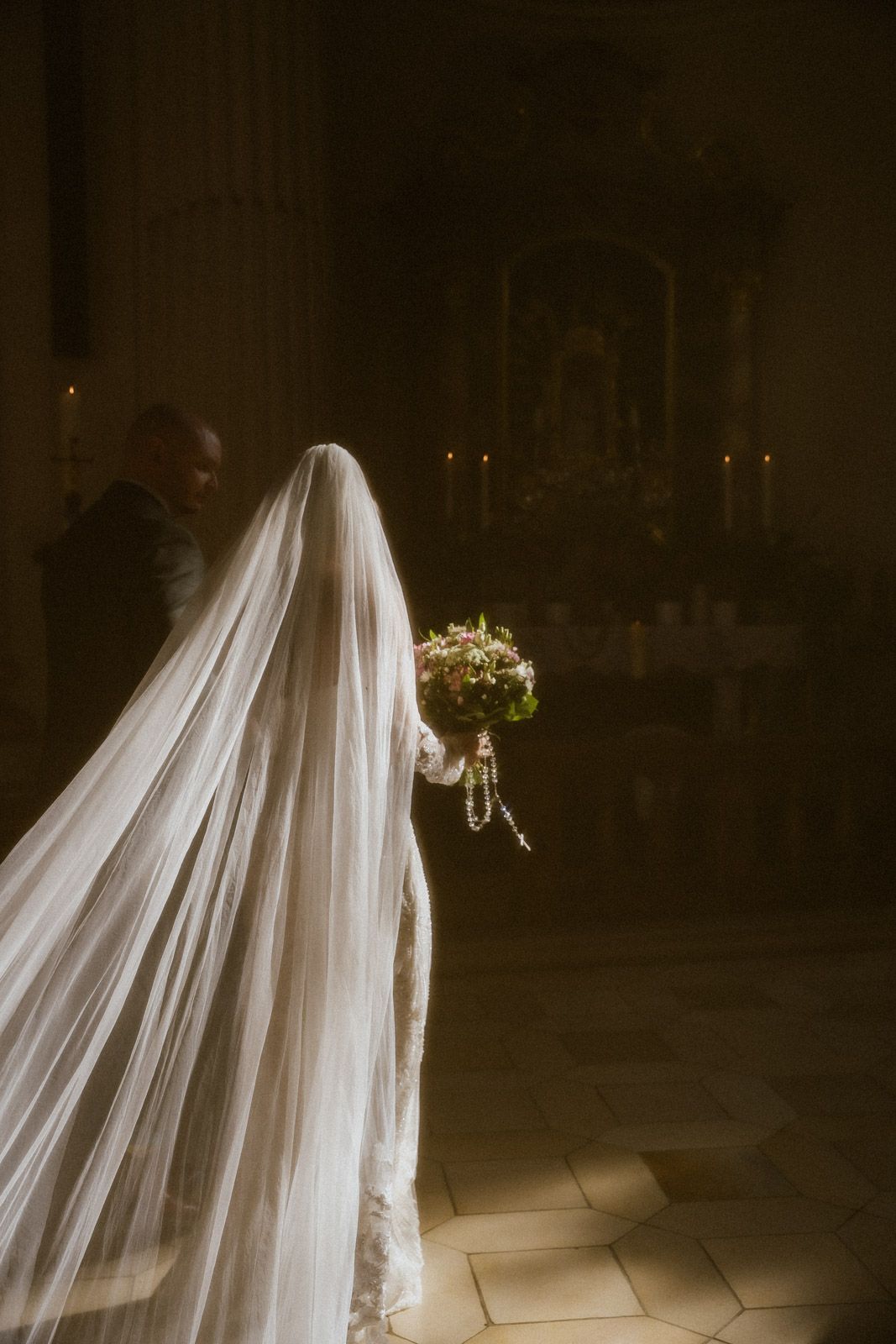 Braut schreitet allein mit Schleier durch eine dunkle Kirche